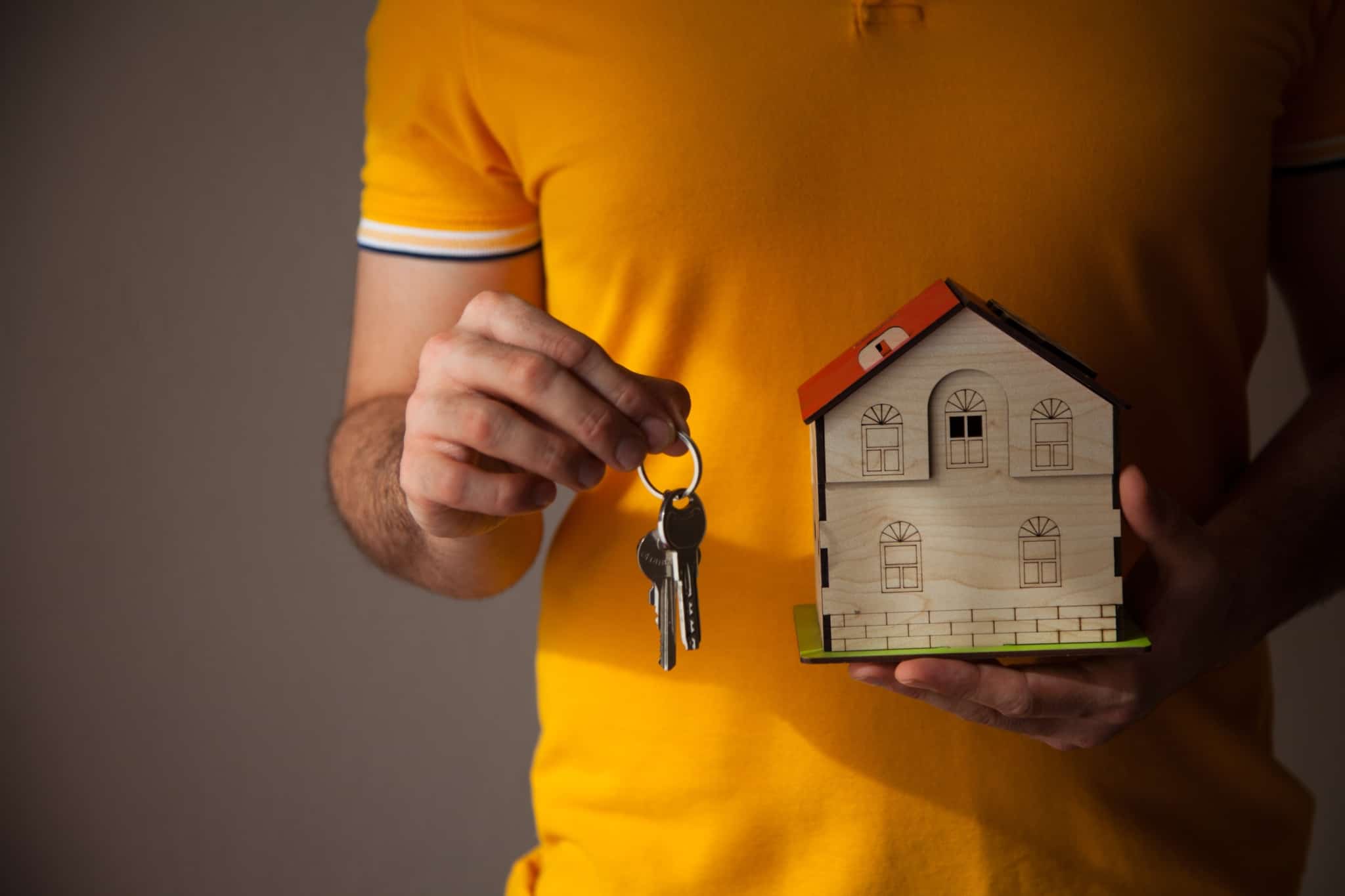 Homem a segurar brinquedo casa de madeira numa mão e uma chave na outra