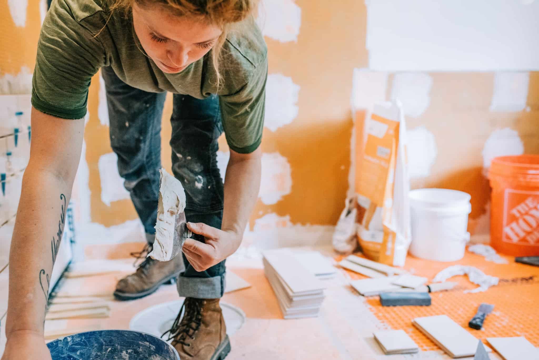 jovem mulher a fazer obras em casa, a aplicar estuque e rodeada de ferramentas e produtos para as obras