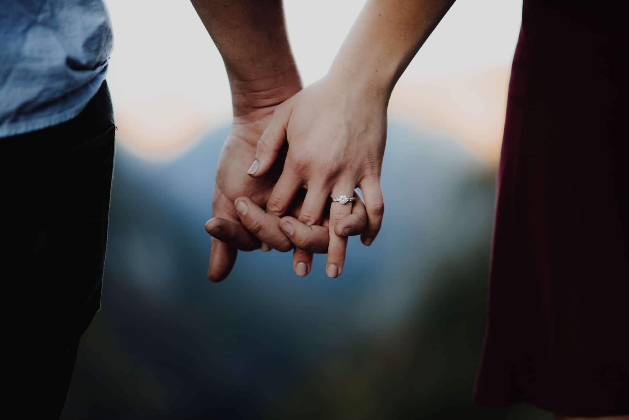 produção fotográfica que mostra apenas as mãos dadas de um jovem casal, com a mulher a mostrar o anel de noivado