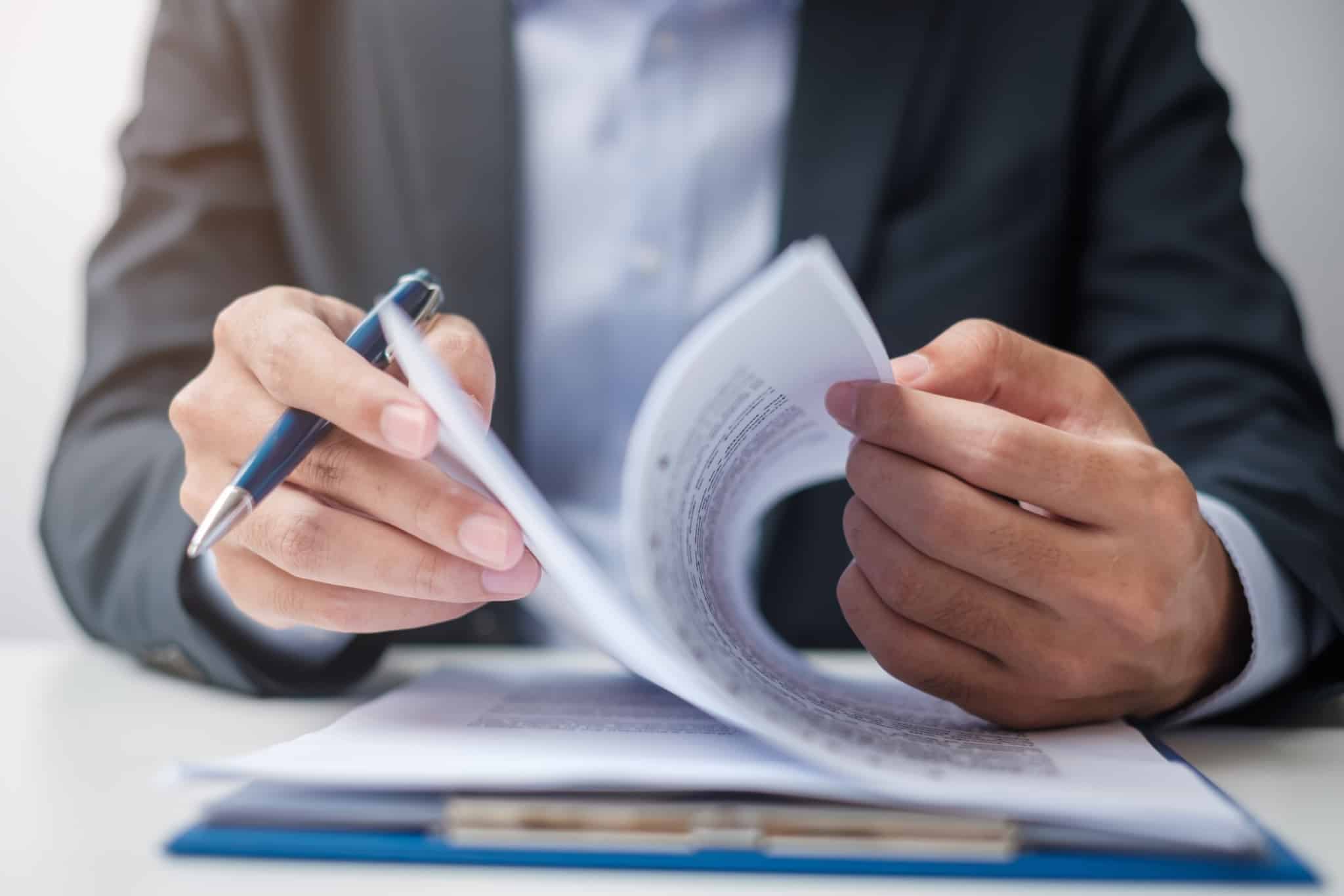 Imagem de uma pessoa sentada à mesa a folhear um contrato de crédito - analisar taxas de juro tan e taeg