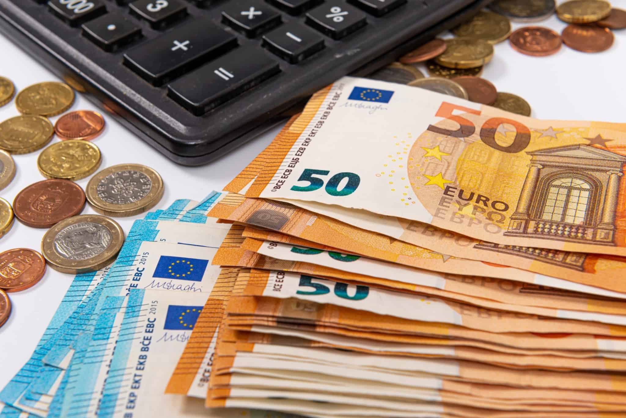 molhos de notas de 50 e 20 euros e algumas moedas ao redor de uma calculadora