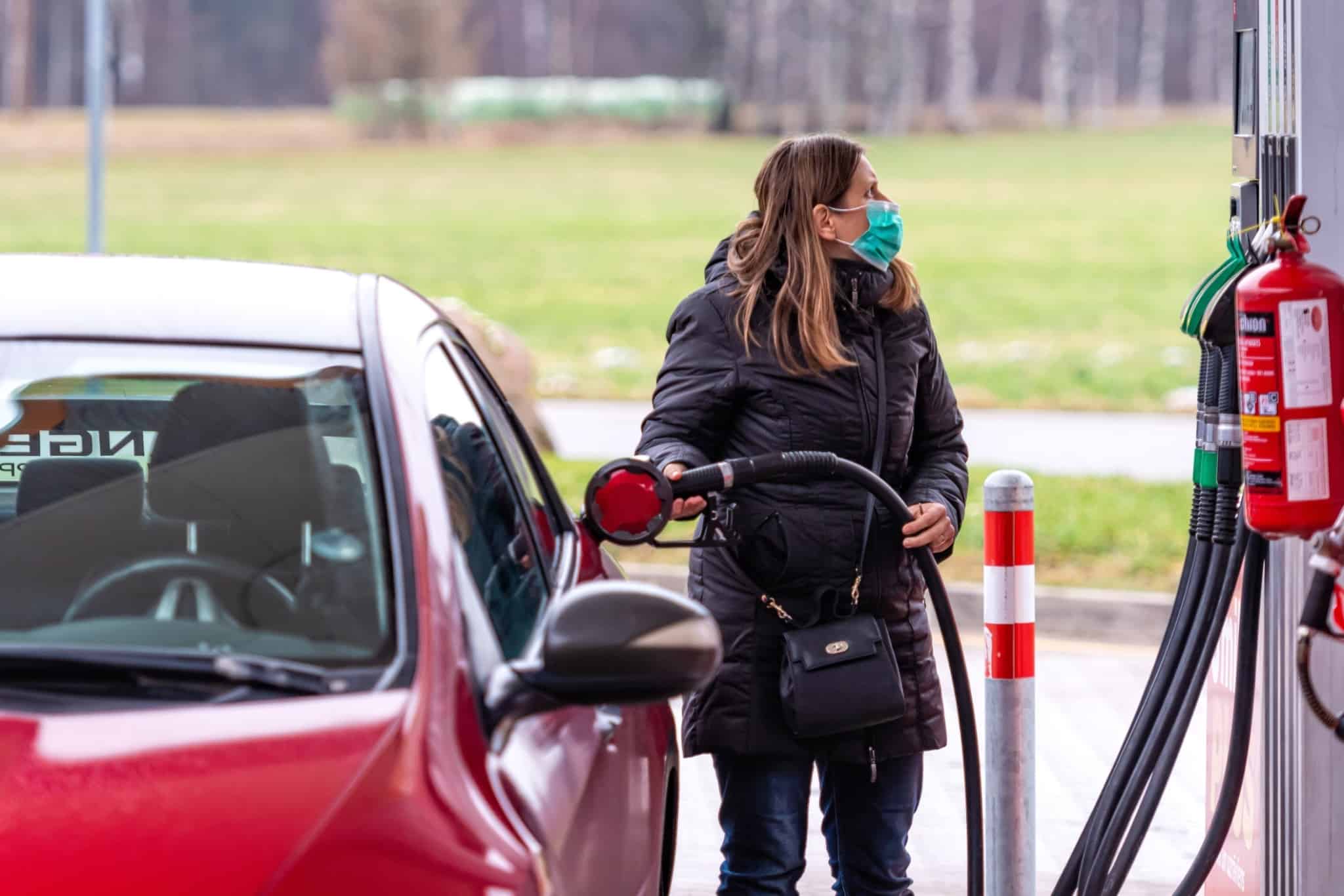 jvem mulher a abastecer o seu carro numa bomba de gasolina (está a usar a máscara de proteção Covid-19)