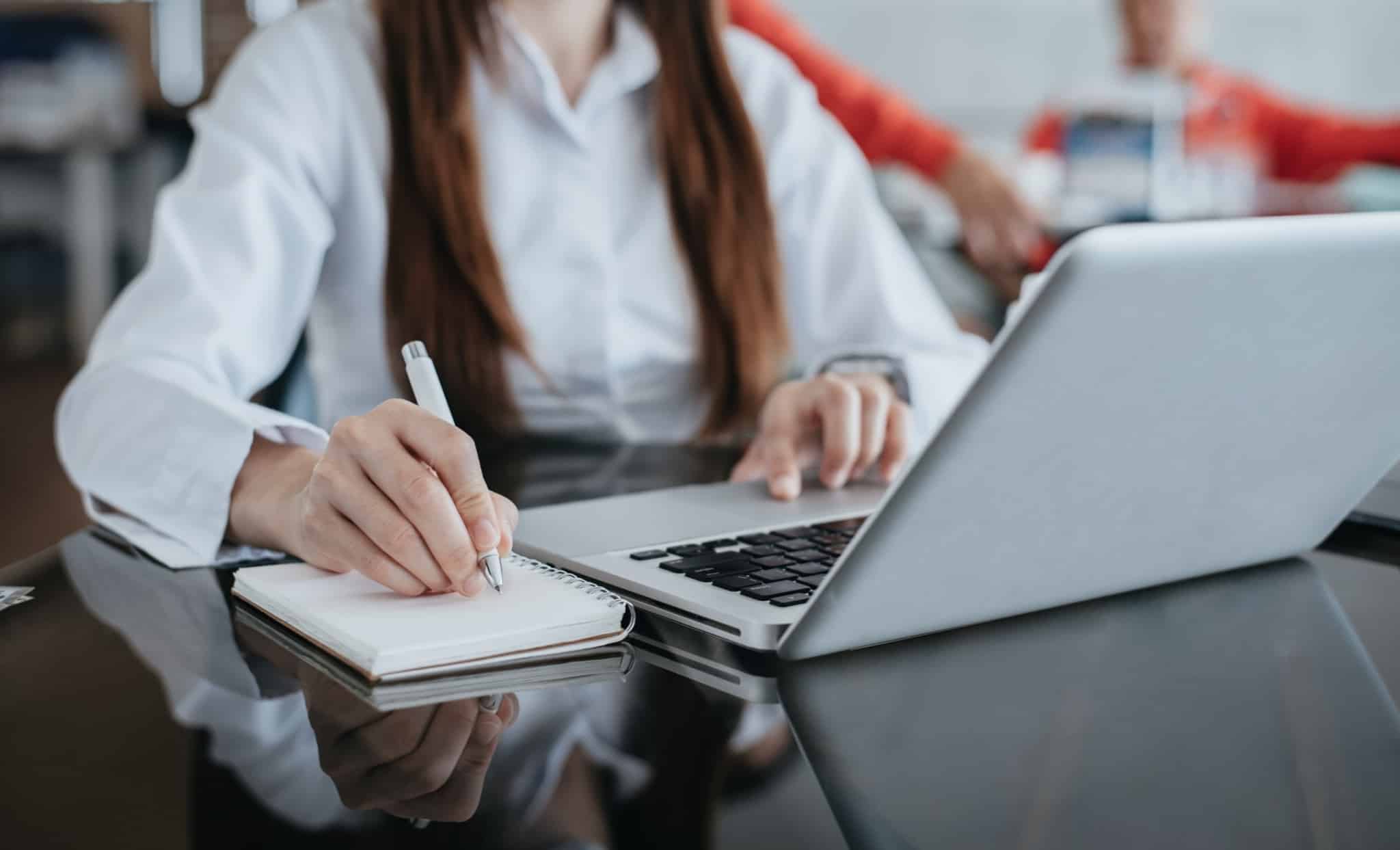 jovem mulher usa o computador portátil para ar ordem para débito direto no pagamento de impostos, enquanto tira notas para um caderno