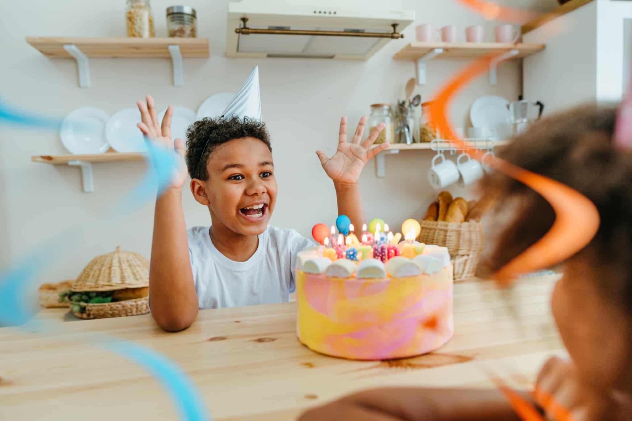 criança, de grande sorriso, a festehar o seu aniversário, prepara-se para soprar as velas do seu bolo