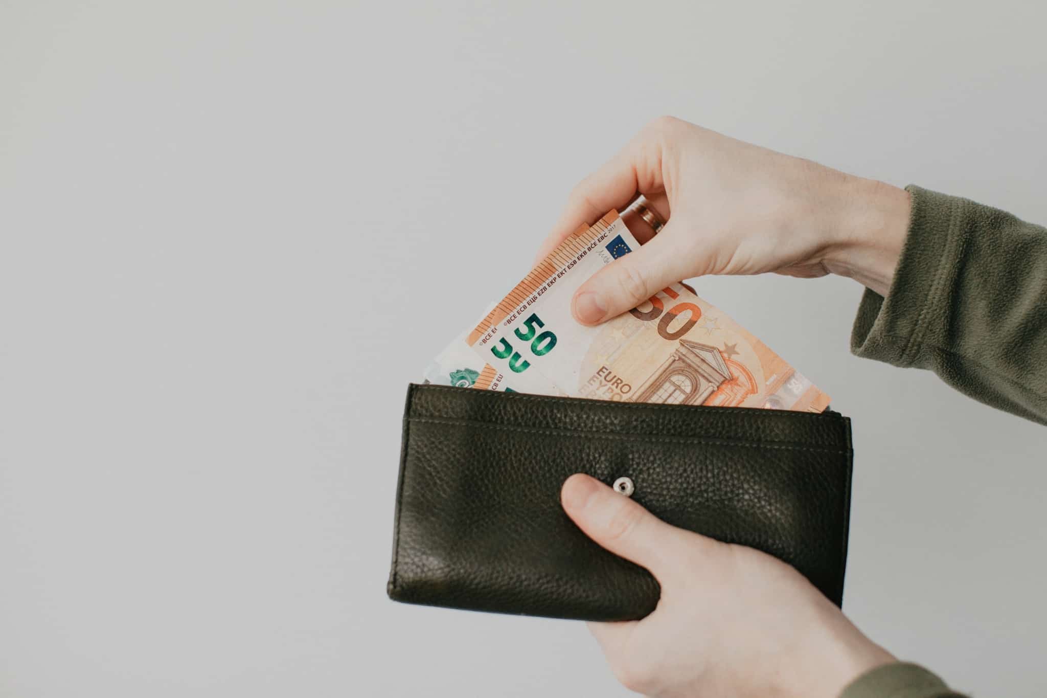 produção fotográfica com uma mão de uma jovem mulher a segurar uma carteira onde coloca e vai juntando notas de 5o euros