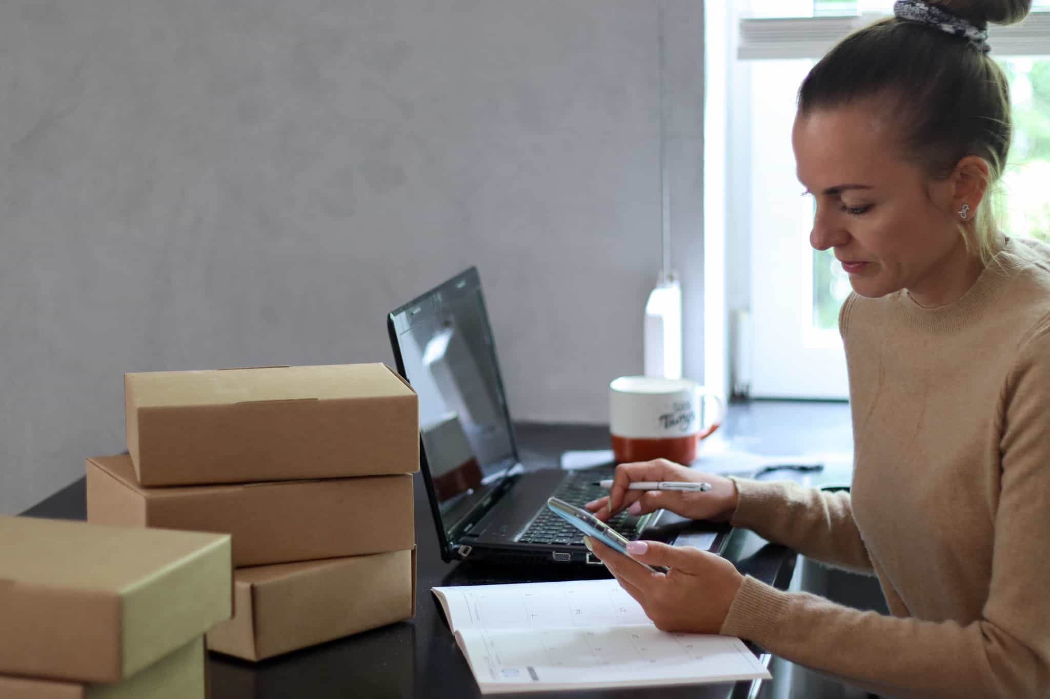 jovem mulher consulta telemóvel e computador portátil para gerir o seu negócio com que vai ganhar dinheiro online