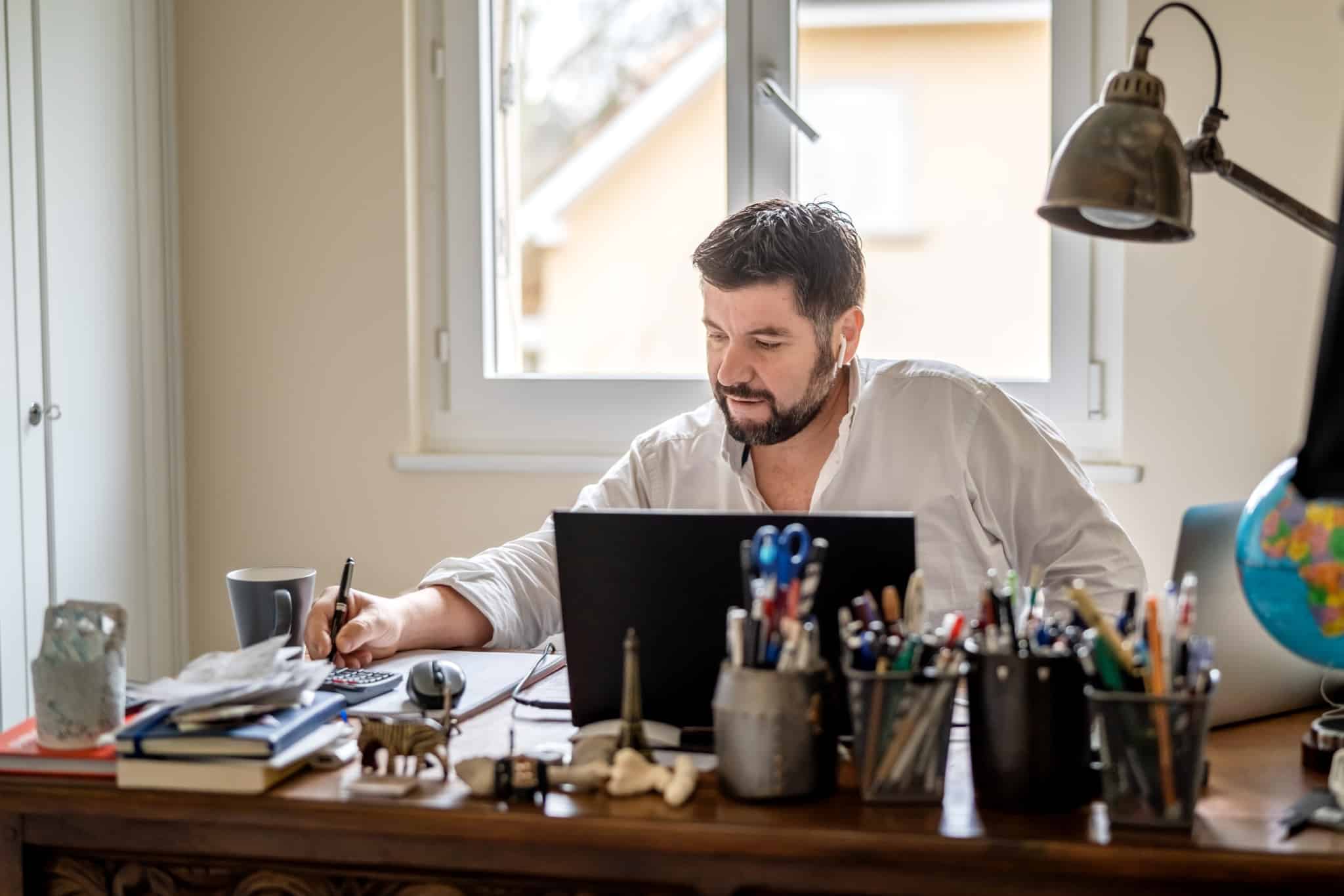 homem sentado à secretária frente ao computador a fazer contas