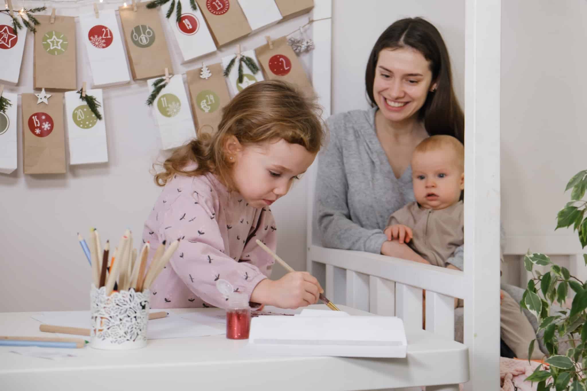 criança a pintar com uma adulta com um bebé ao colo a ver