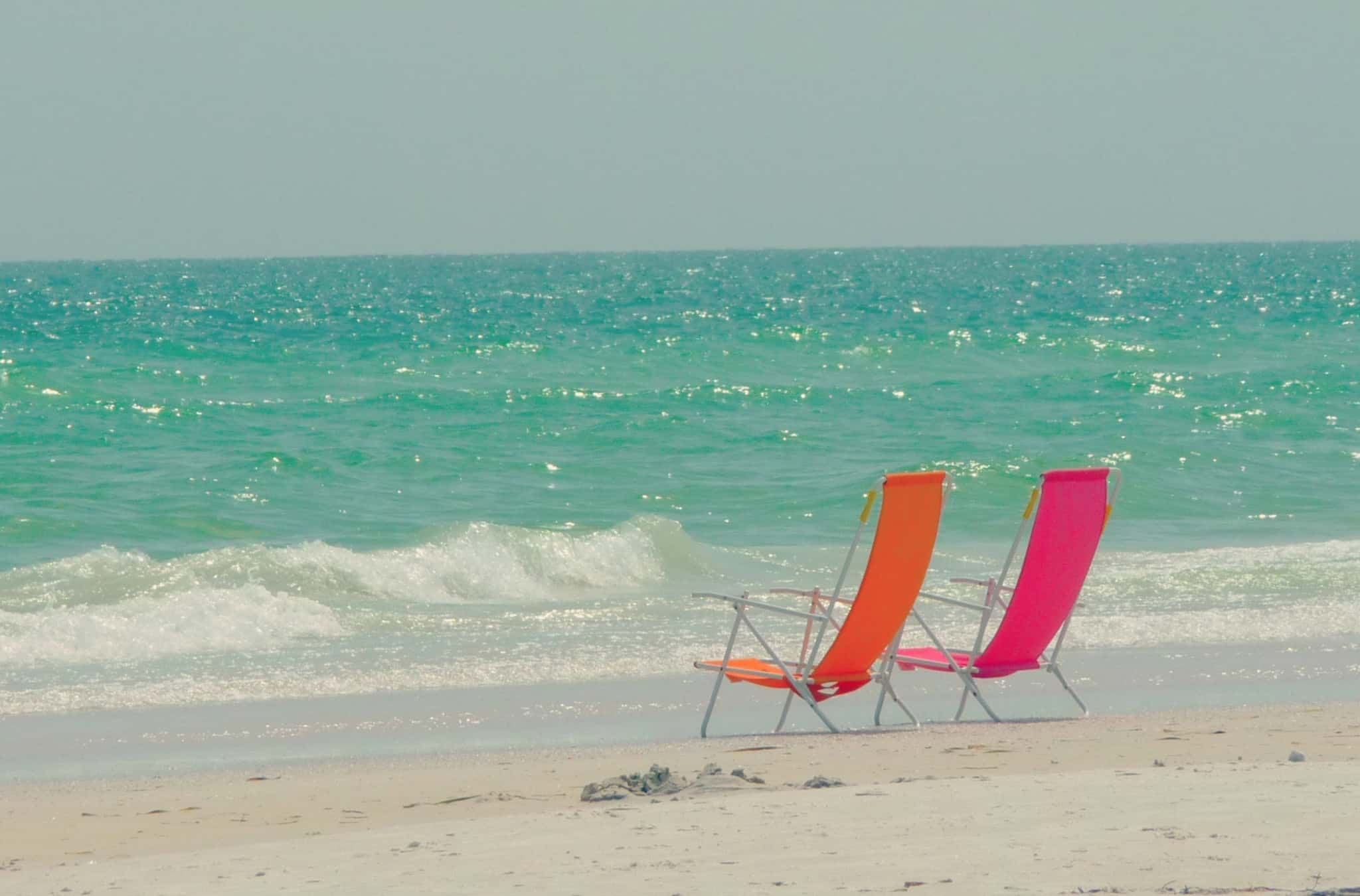 duas cadeiras de praia, uma laranja e outra rosa, colocadas à beira mar, na praia, um local de sonho para uma reforma que deve ser construída com base em estratégias de poupar