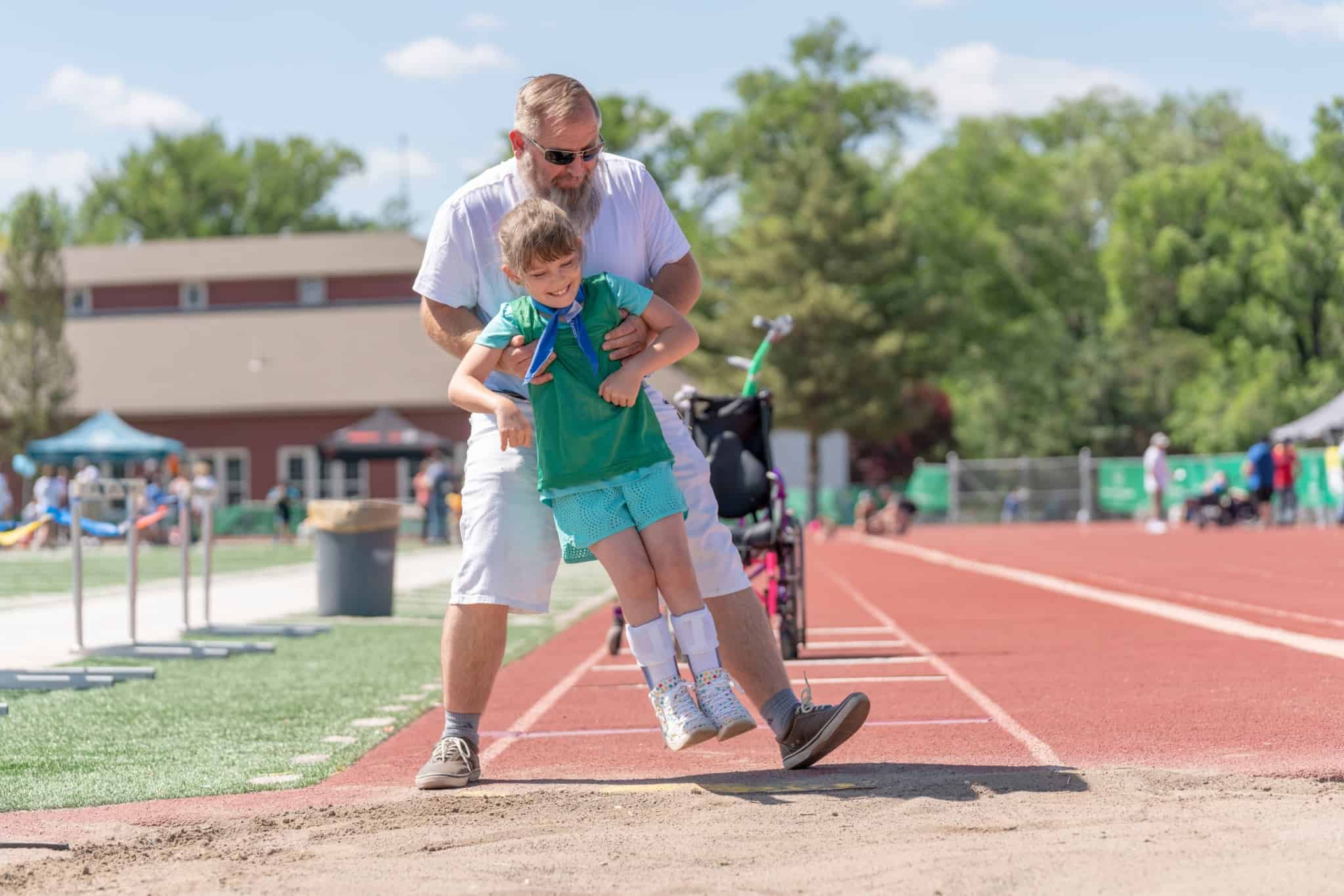 pai e filha pequena, a receber subsídio de educação especial, tentam numa pista de corrida fazer alguns exerícios físicos