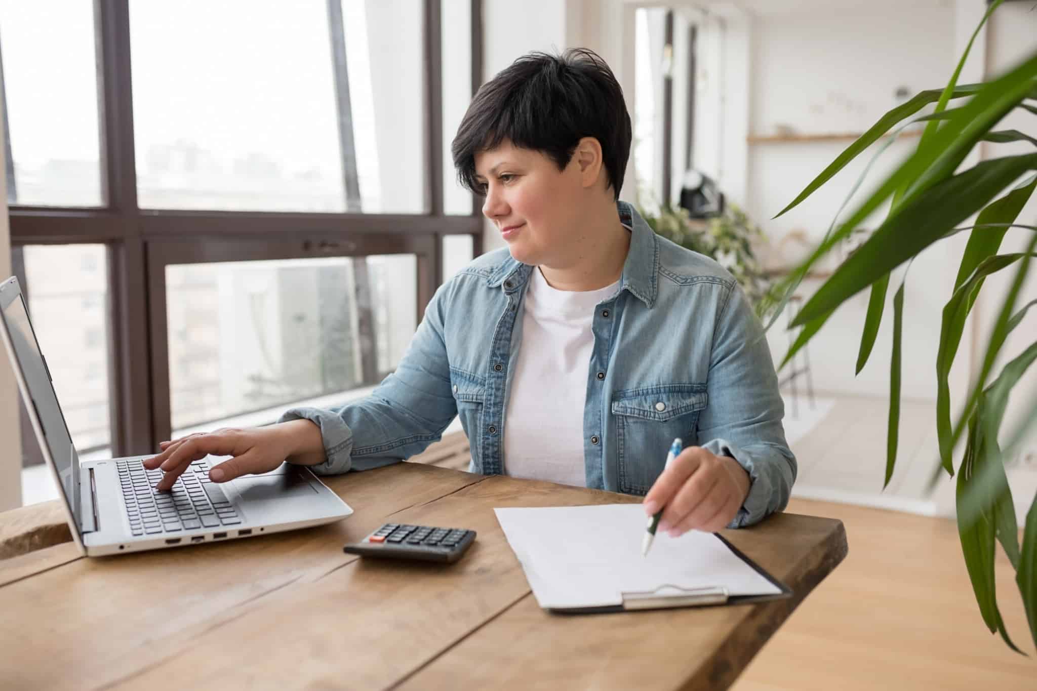jovem mulher a afzer contas, usando o caderno, o computador e a máquina de calcular para preencher a declaração de IVA