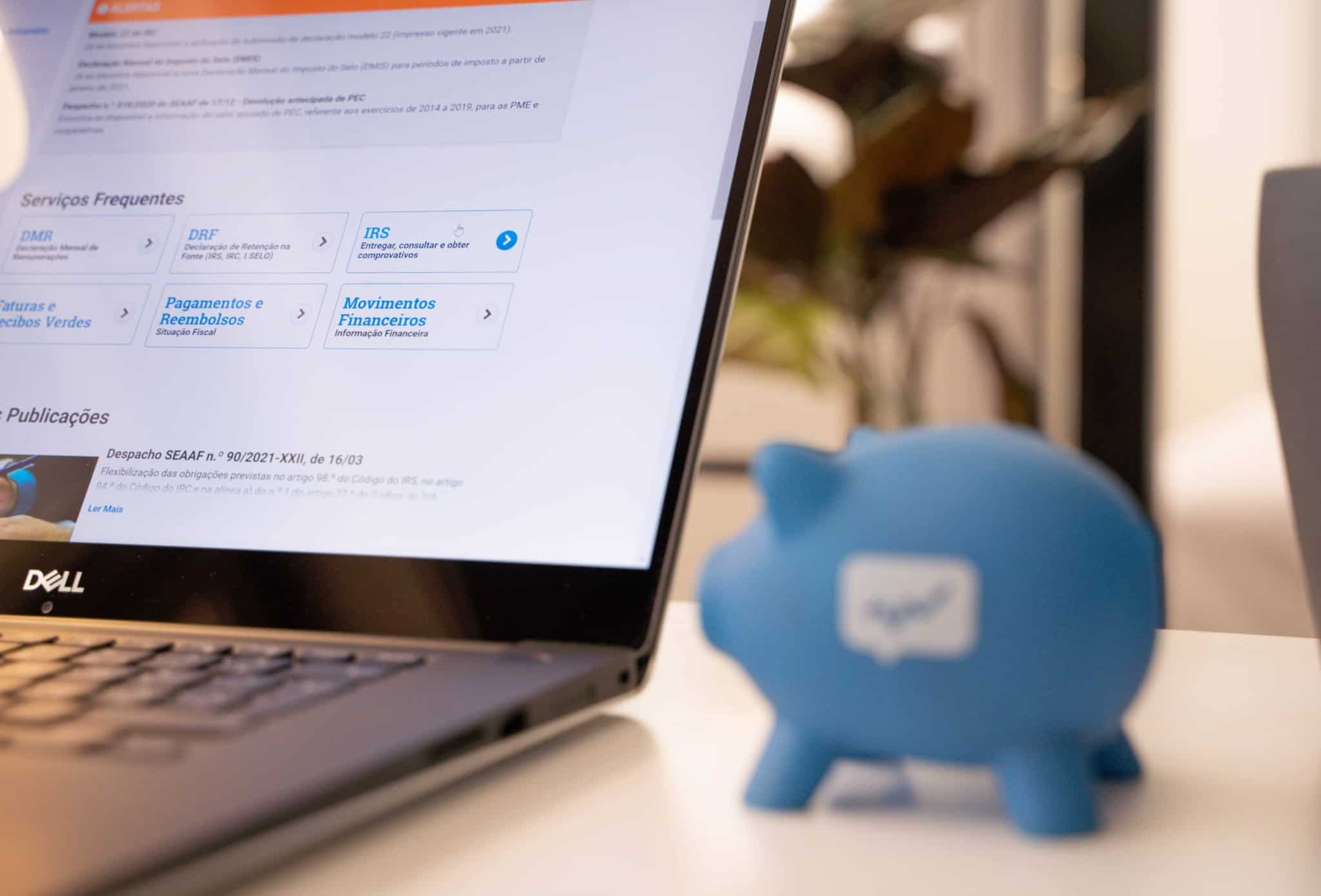 Imagem de um porquinho mealheiro azul e de um computador portátil na página do Portal das Finanças numa alusão à entrega do IRS em 2022