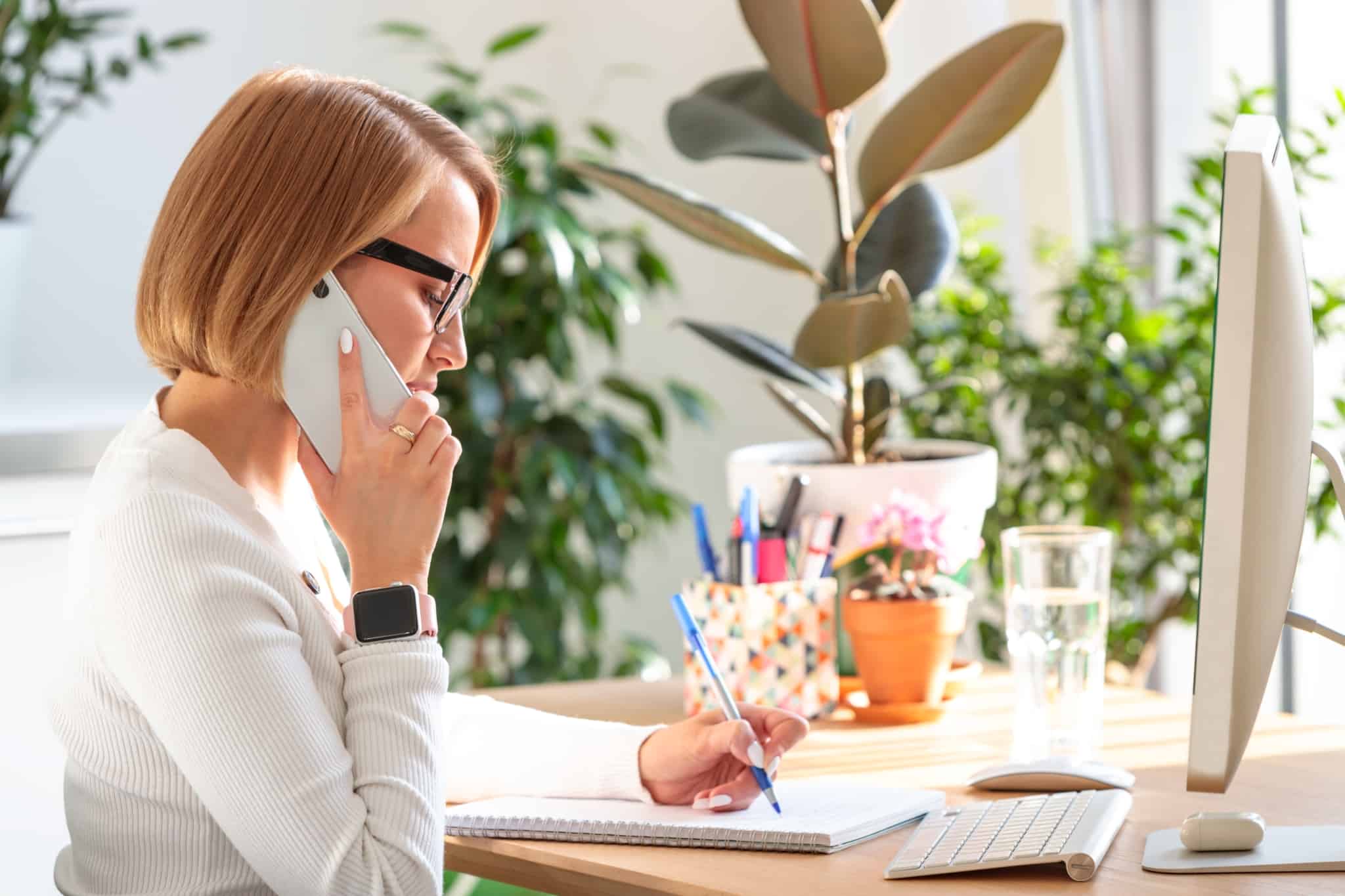 mulher ao telefone sentada à frente do computador a trabalhar como prestadora de serviços no seu primeiro emprego