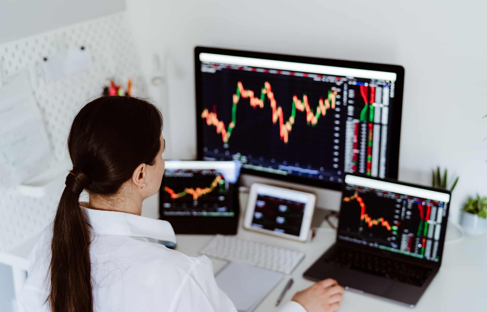 mulher em frente a vários ecrãs com gráficos de investimentos e a analisar as mais-valias em investimentos para preencher o anexo E do IRS