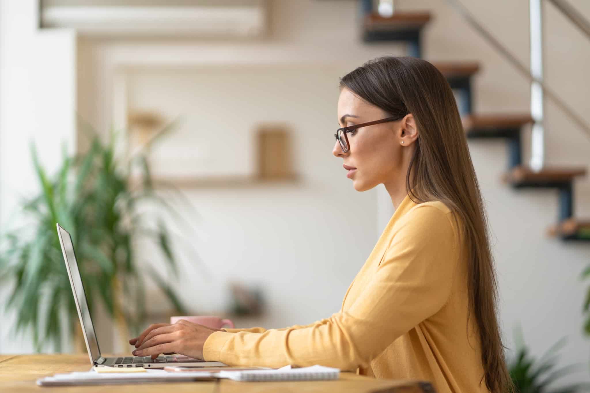 mulher de perfil sentada numa secretária em frente ao computador a consultar o Código do Trabalho