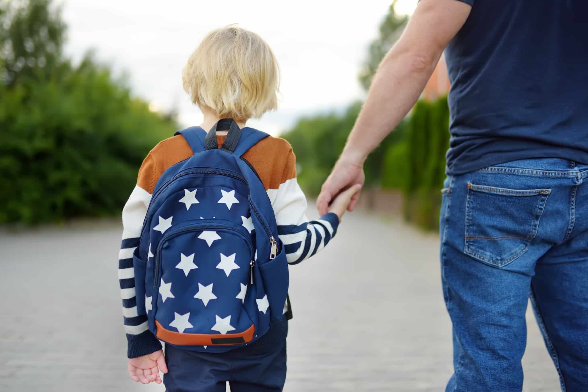 criança com uma mochila de mão dada com o pai a ir na ida para o primeiro ciclo