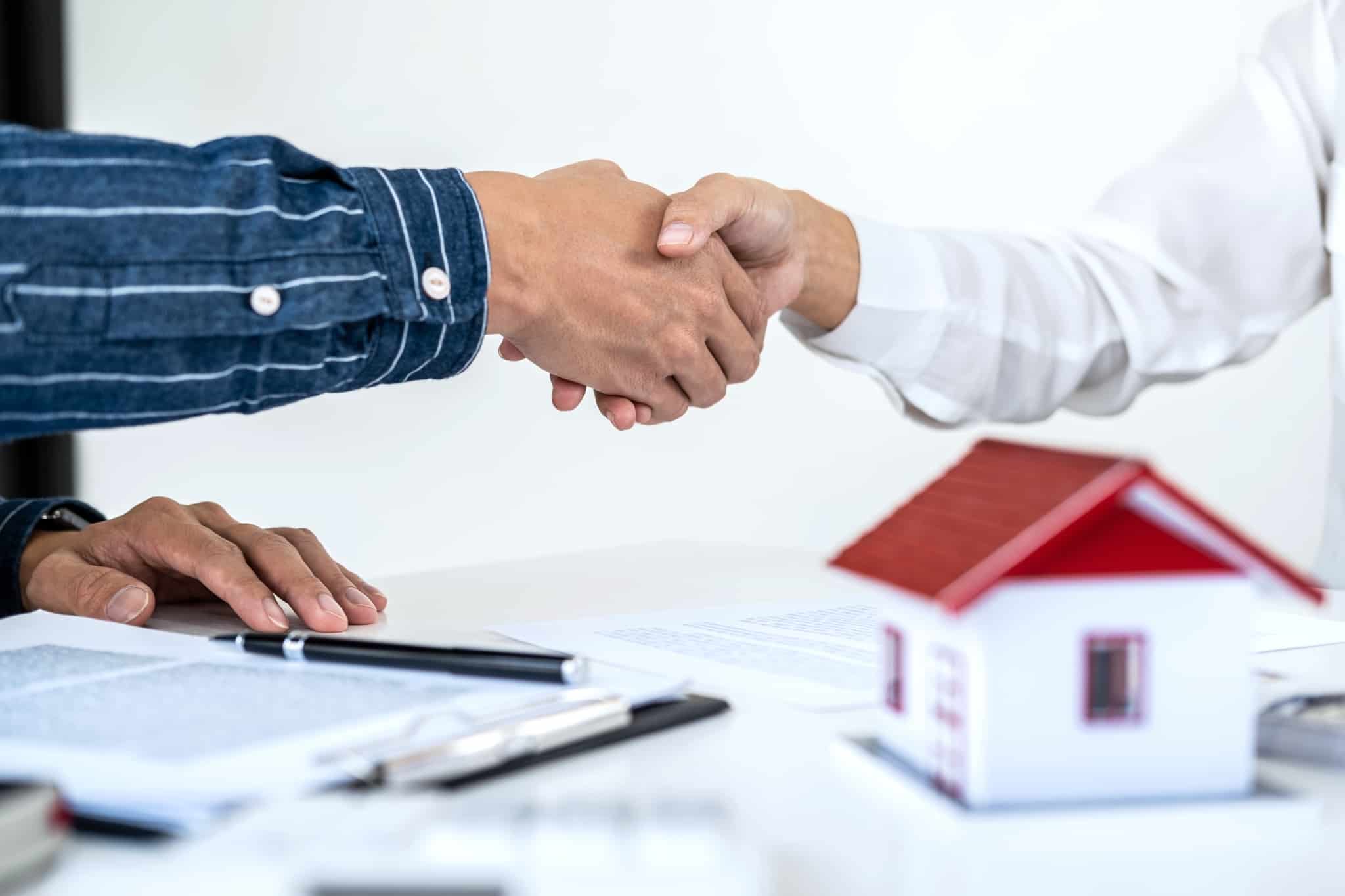 Aperto de mão entre senhores com contrato crédito habitação em cima da mesa e casa de madeira