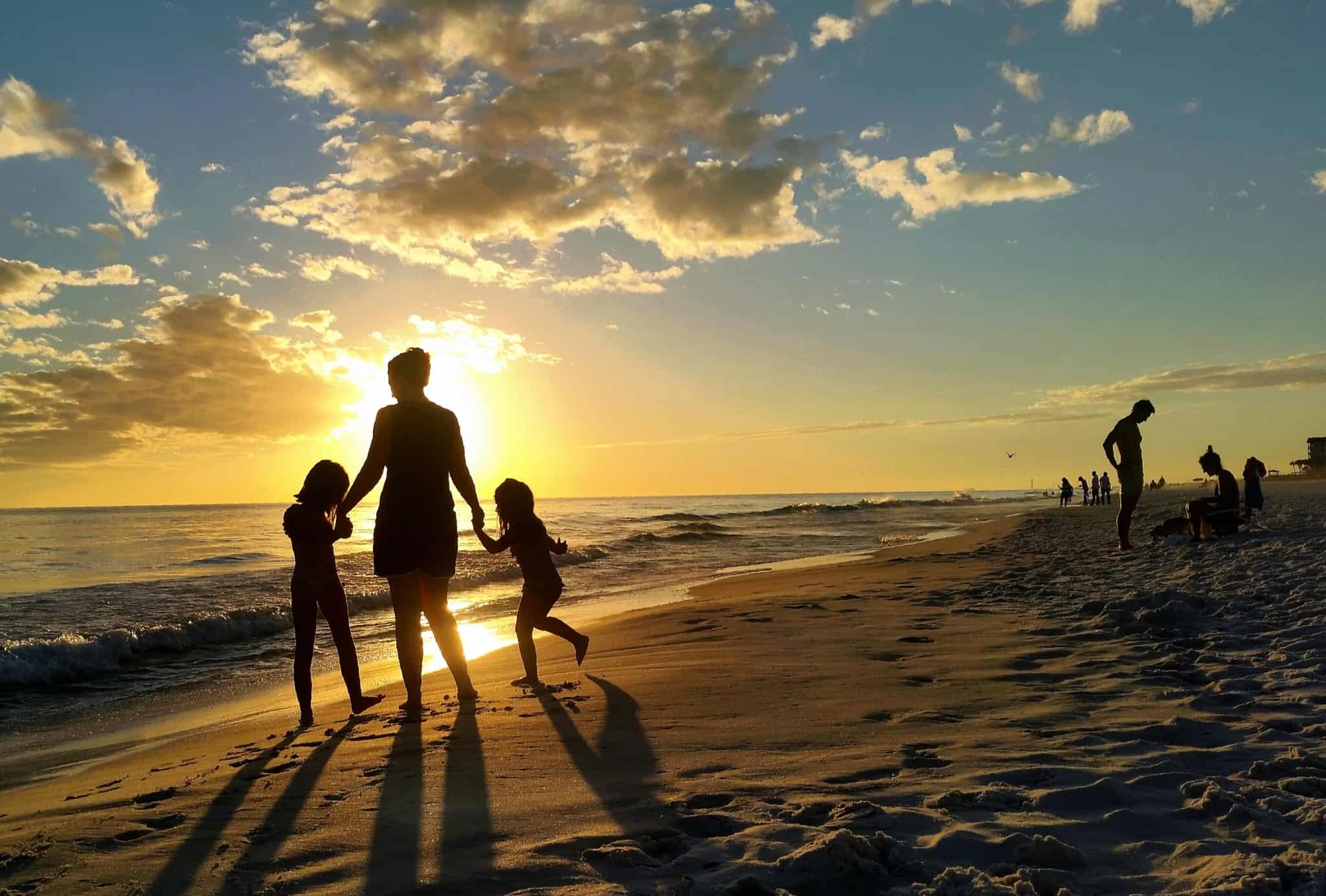 jovem mulher, com seguro de vida, com duas crianças pela mão caminham no areal da praia ao por do sol