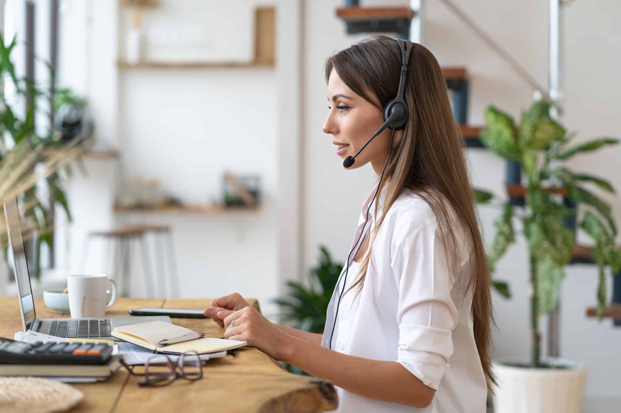 jovem mulher a trabalhar em casa, em teletrabalho, a falar com phones e a usar o computador