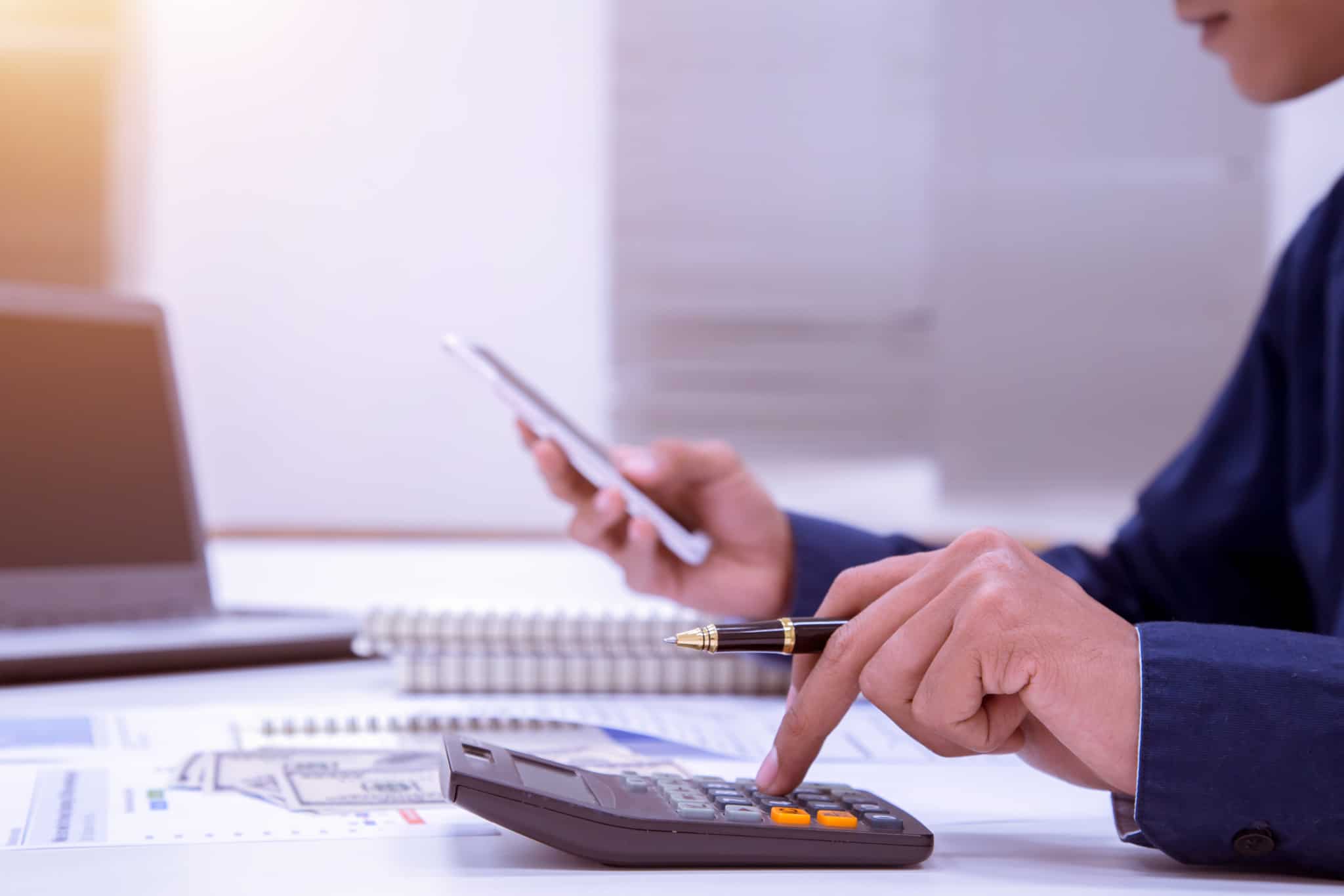 Homem consulta informação no sue telemóvel e faz contas numa máquina de calcular, avaliando o retorno de investimento com base na distribuição de dividendos