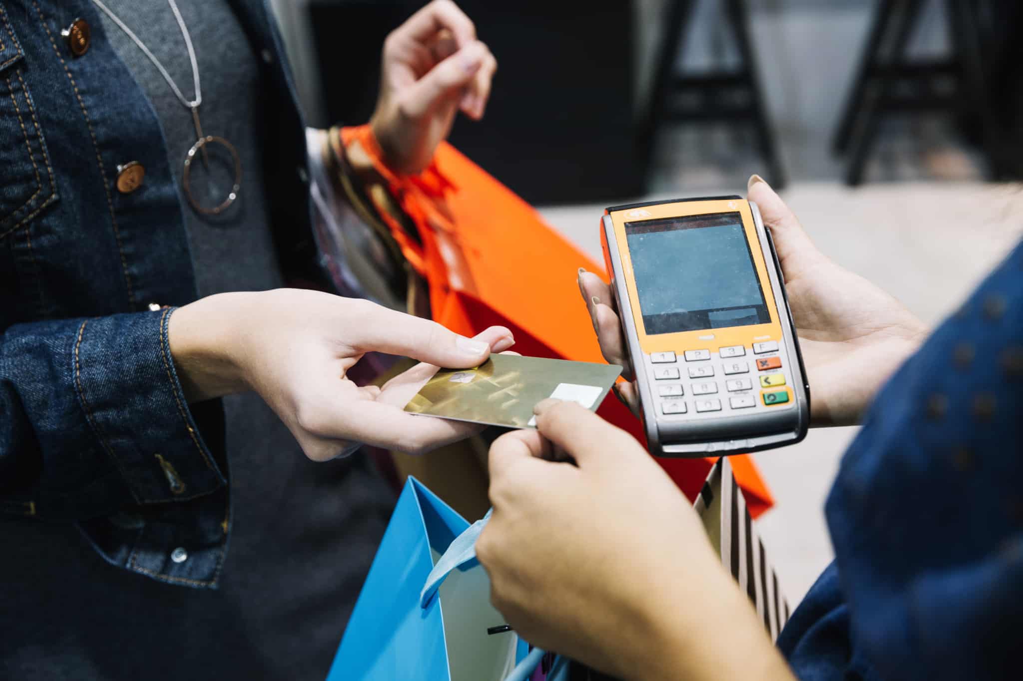 jovem mulher, carregada com sacos de compras nos braços, entrega cartão de crédito para pagar compras