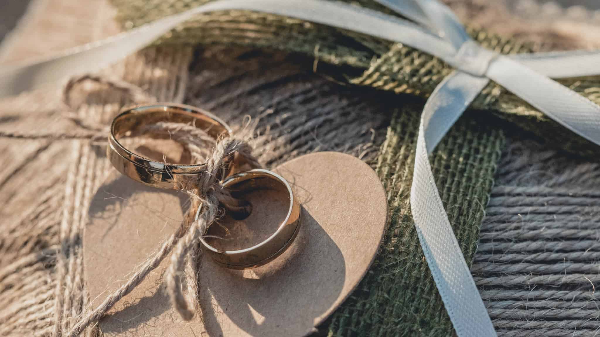 Alianças de casamento douradas unidas por um cordel em baixo de um coração de cartão representando o casamento