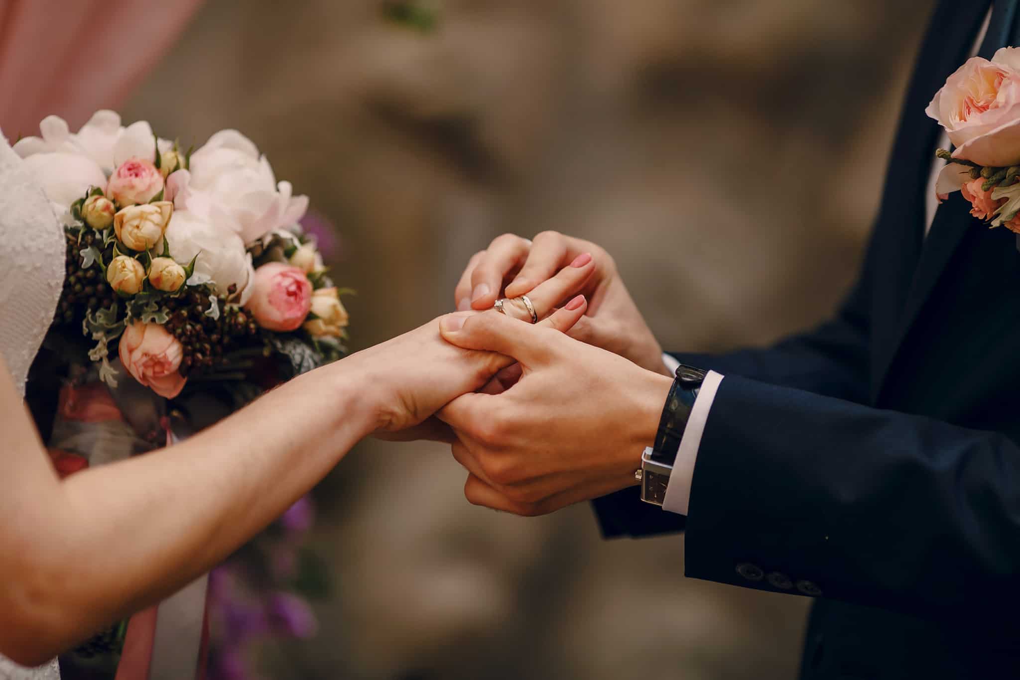 Noivo a colocar anel a noiva com ramo de flores no casamento