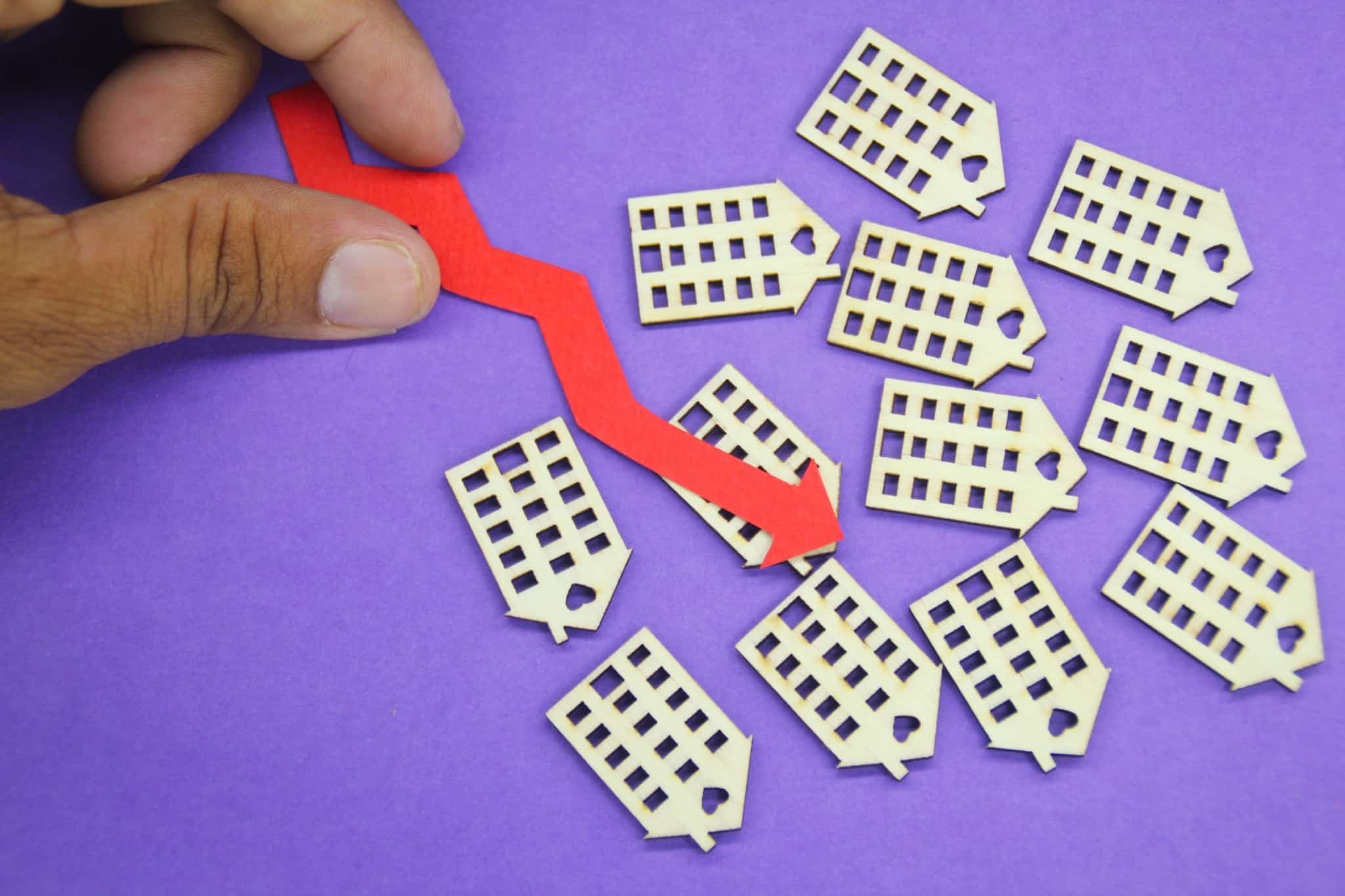 Figuras de prédios em madeira com seta vermelha para baixo simbolizando dívidas de condomínio