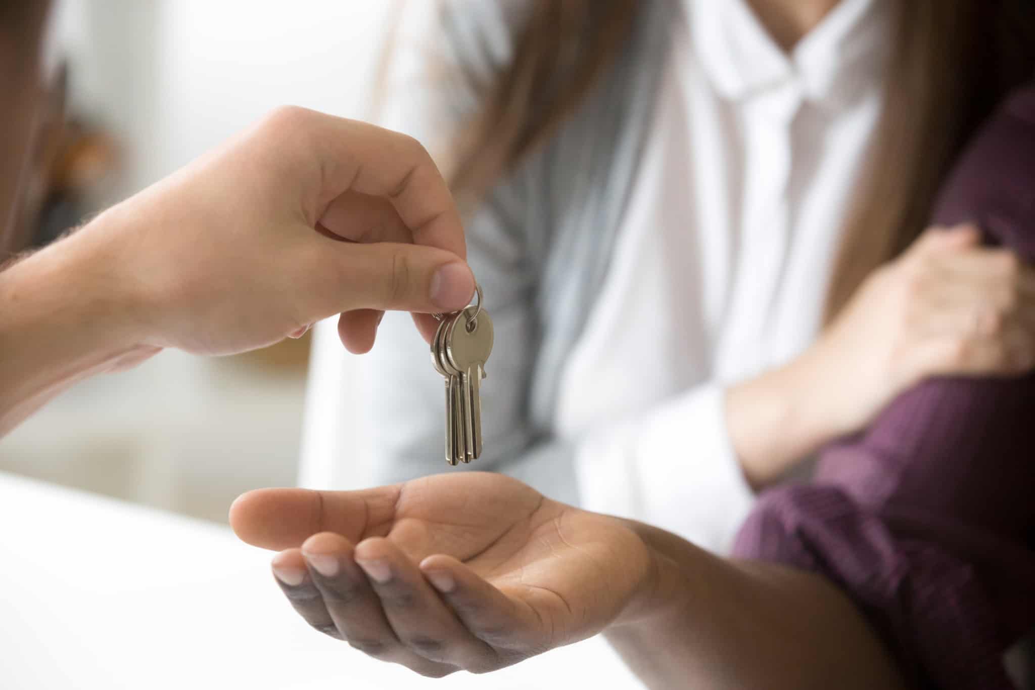 de mão estendida, jovem mulher recebe as chaves do imóvel que comprou e do qual guarda a licença de habitação, entre os documentos obrigatórios que tem de ter