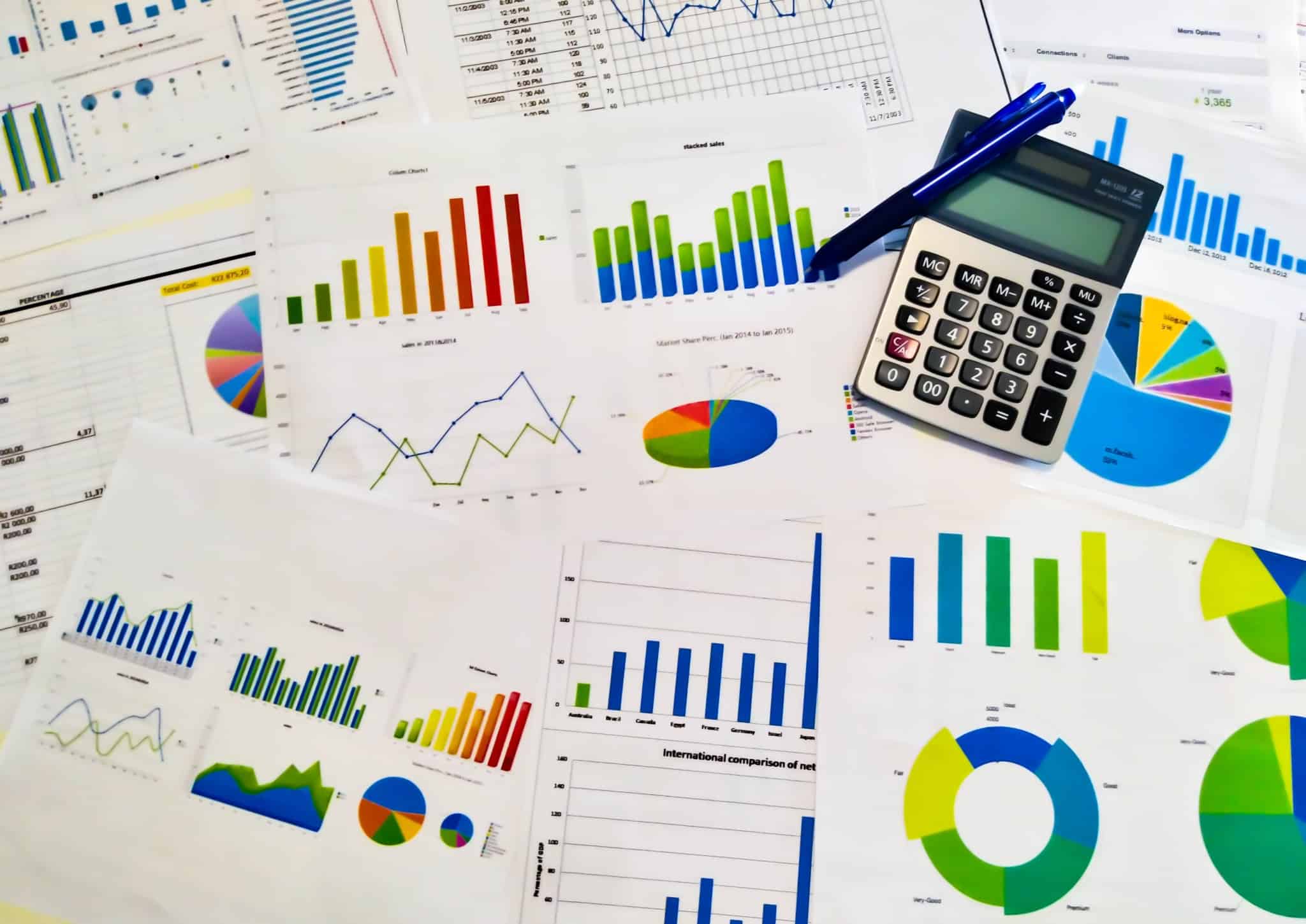 produção fotográfica que mostra um aglomerado de documentos financeiros, com gráficos de muitas cores e feitios, com uma calculadora pousada também nesta mesa, sendo que são referentes ao relatório e contas