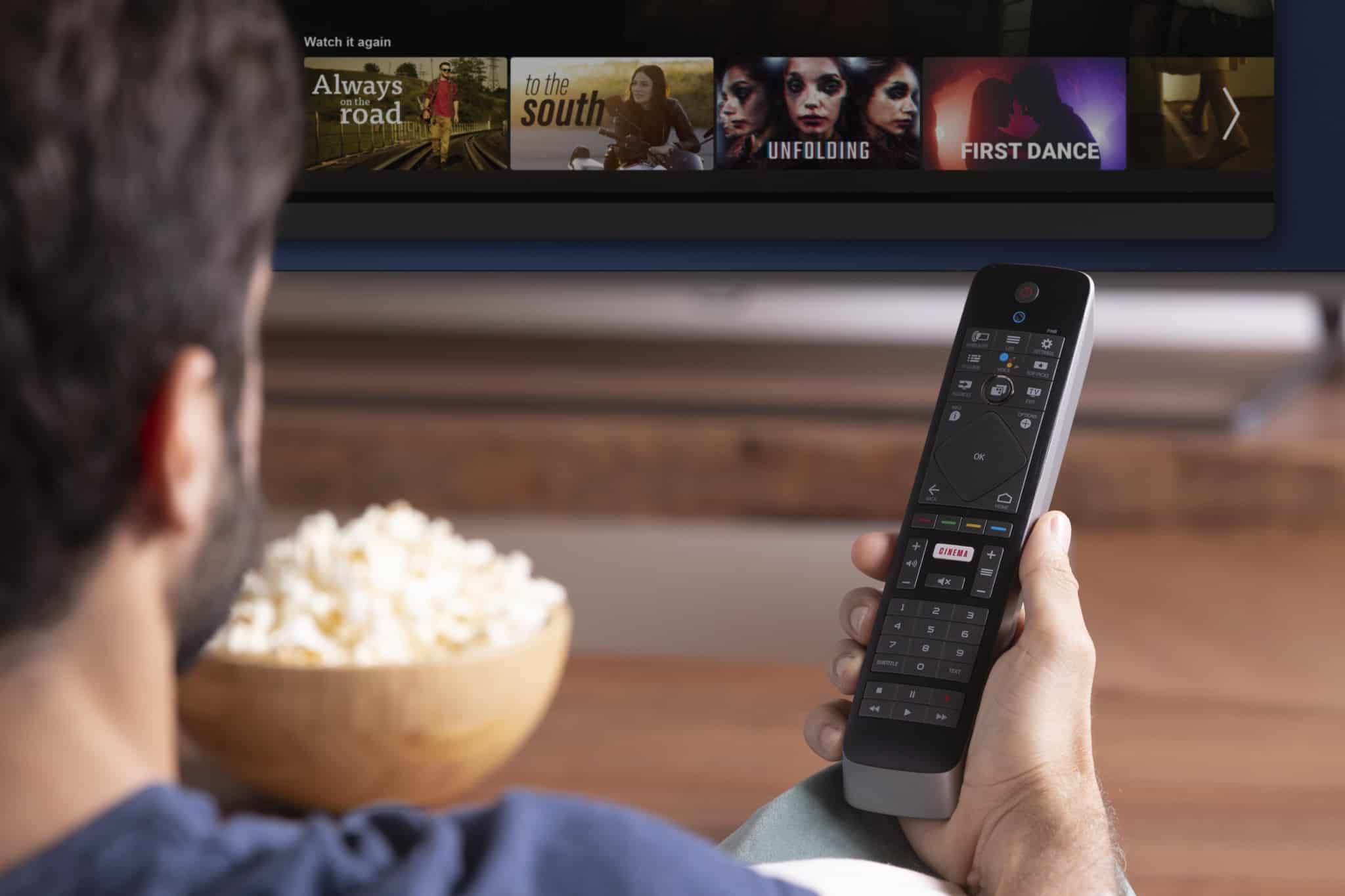 jovem rapaz a ver TV com subscrições, a segurar comando e uma taça de pipocas