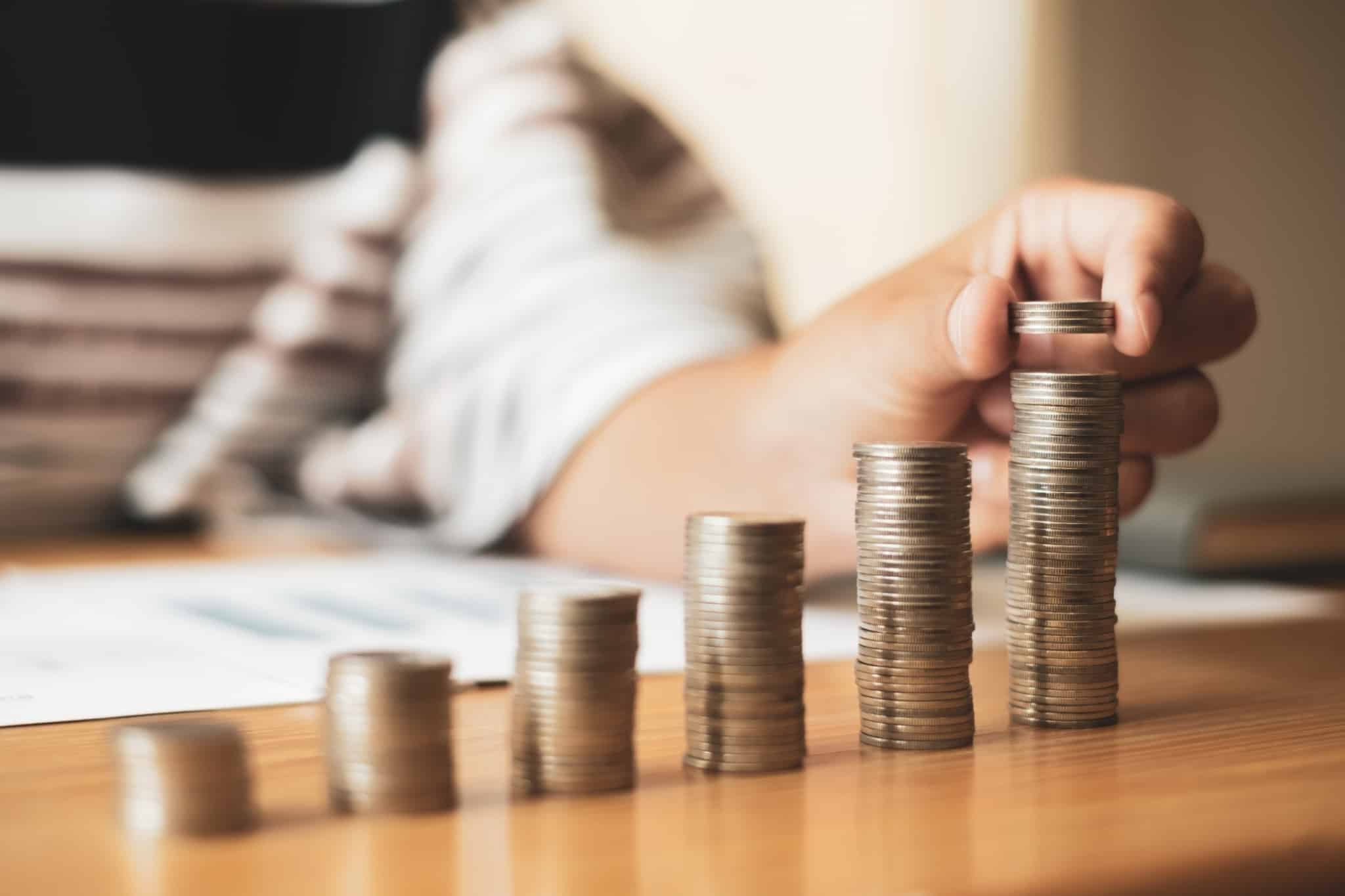 Mão de uma mulher coloca uma moeda no cima de uma torre de moedas