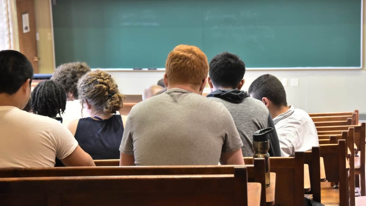 Sala de aulas com alunos sentados a assistir a uma aula