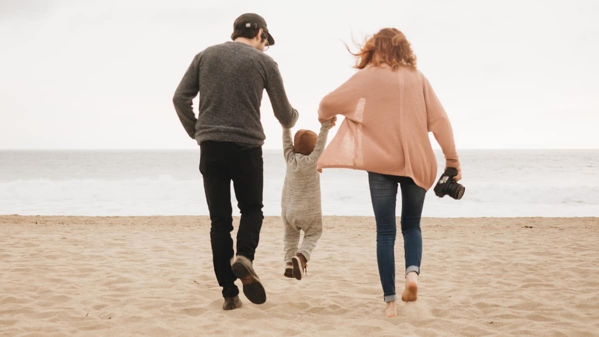 Pai e mãe a dar as mãos ao filho na praia durante as férias