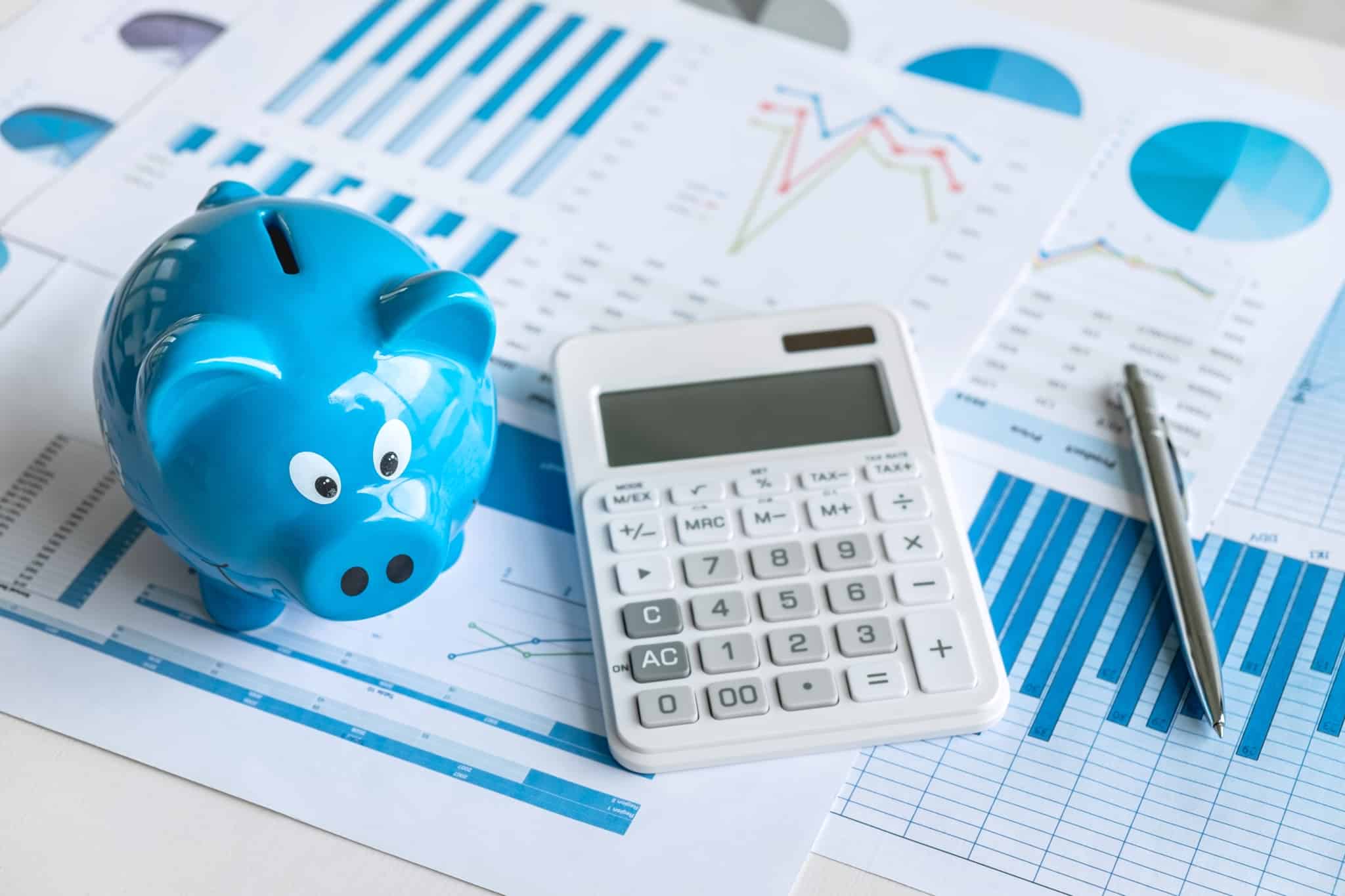 um porquinho mealheiro azul ao lado de uma calculadora e uma caneta, sob documentos com gráficos que mostram as oscilações dos investimentos em PPR FPR Certificados de Reforma