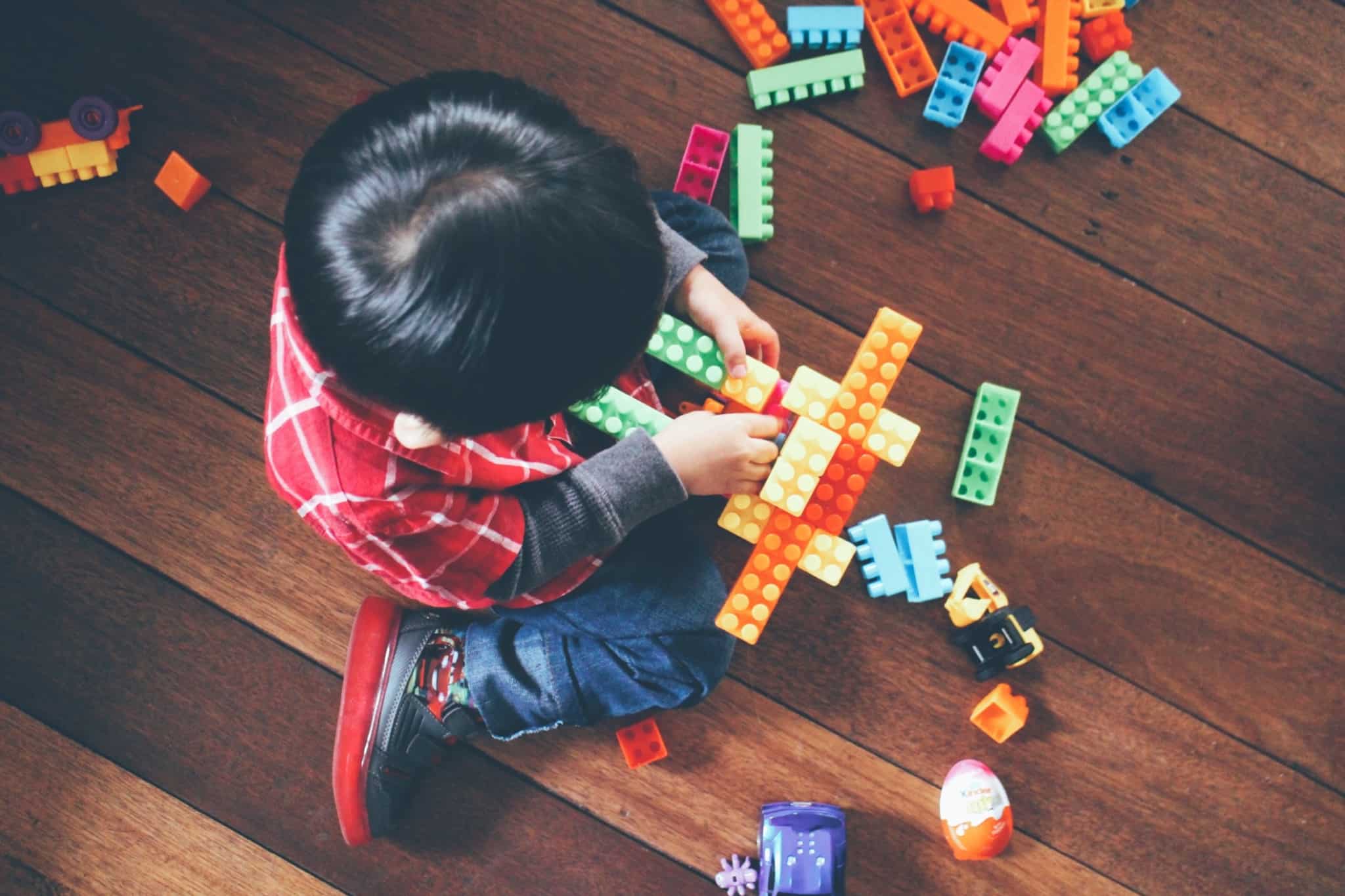 criança, com direito a bonificação do abono de família que apoia crianças com deficiência, no chão a brincar entre uma série de peças Lego