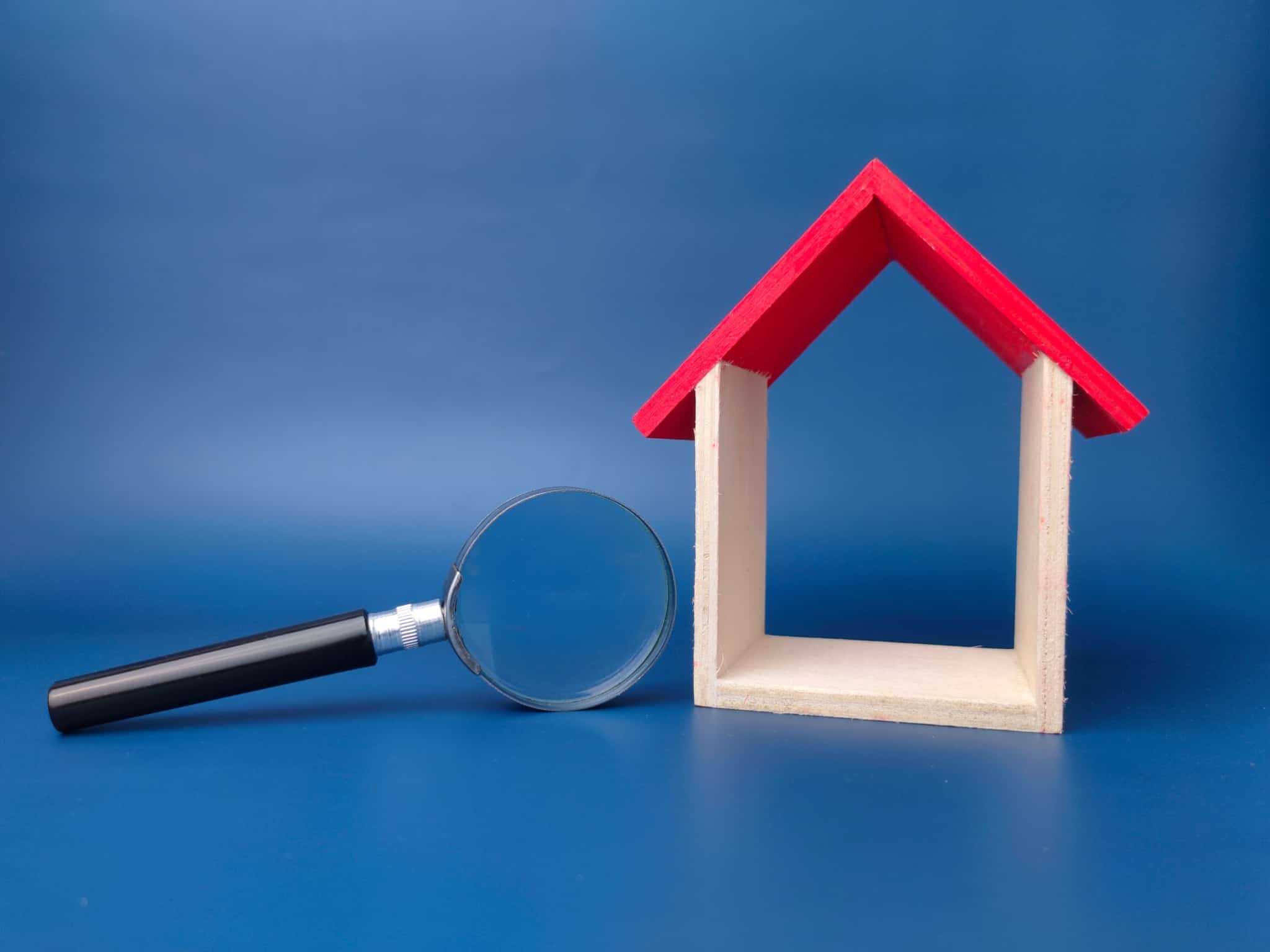 em fundo azul uma maqueta de uma casa só com paredes e teto , junto a uma lupa, ilustram as questões do crédito habitação e quando renegociar