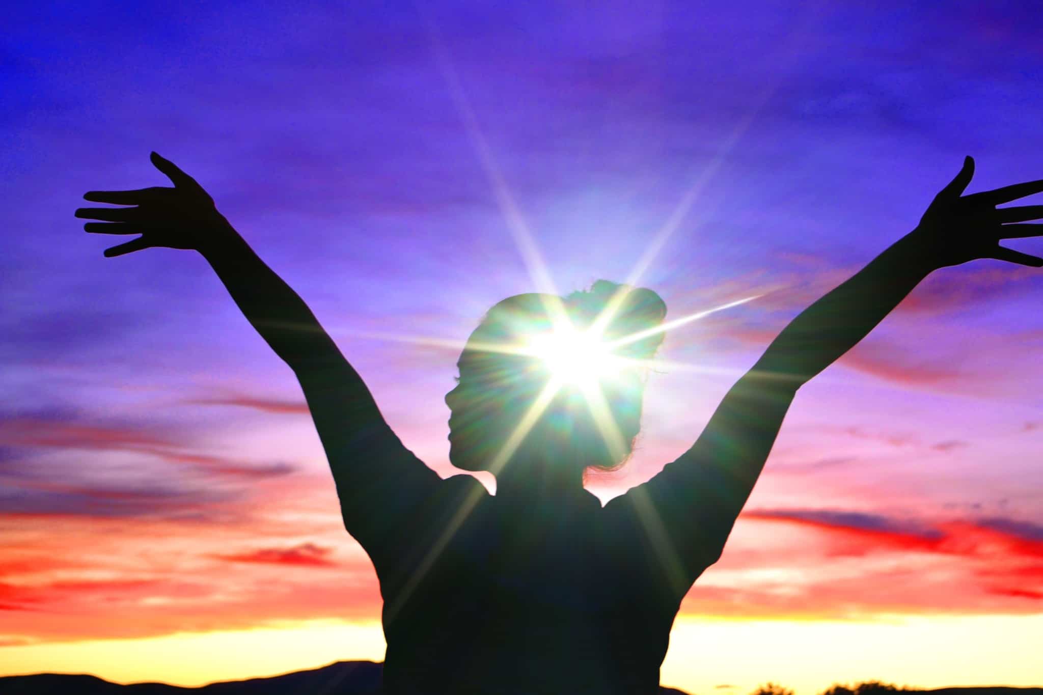 jovem mulher, em contra luz, num horizonte de cores garridas, eleva os braços e foca-se para descansar o cérebro e preservar a saúde mental