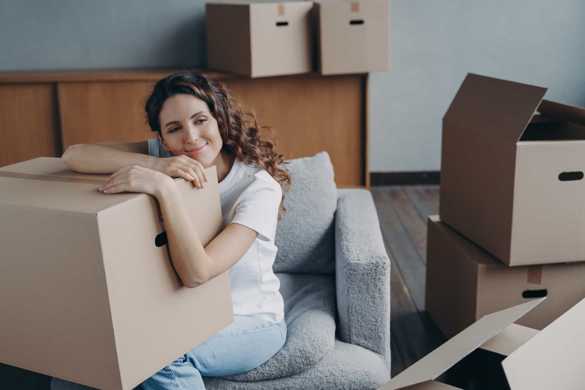 jovem com uma expressão de felicidade agarrada a uma caixa de mudanças, contente por ter decidido comprar casa sozinha