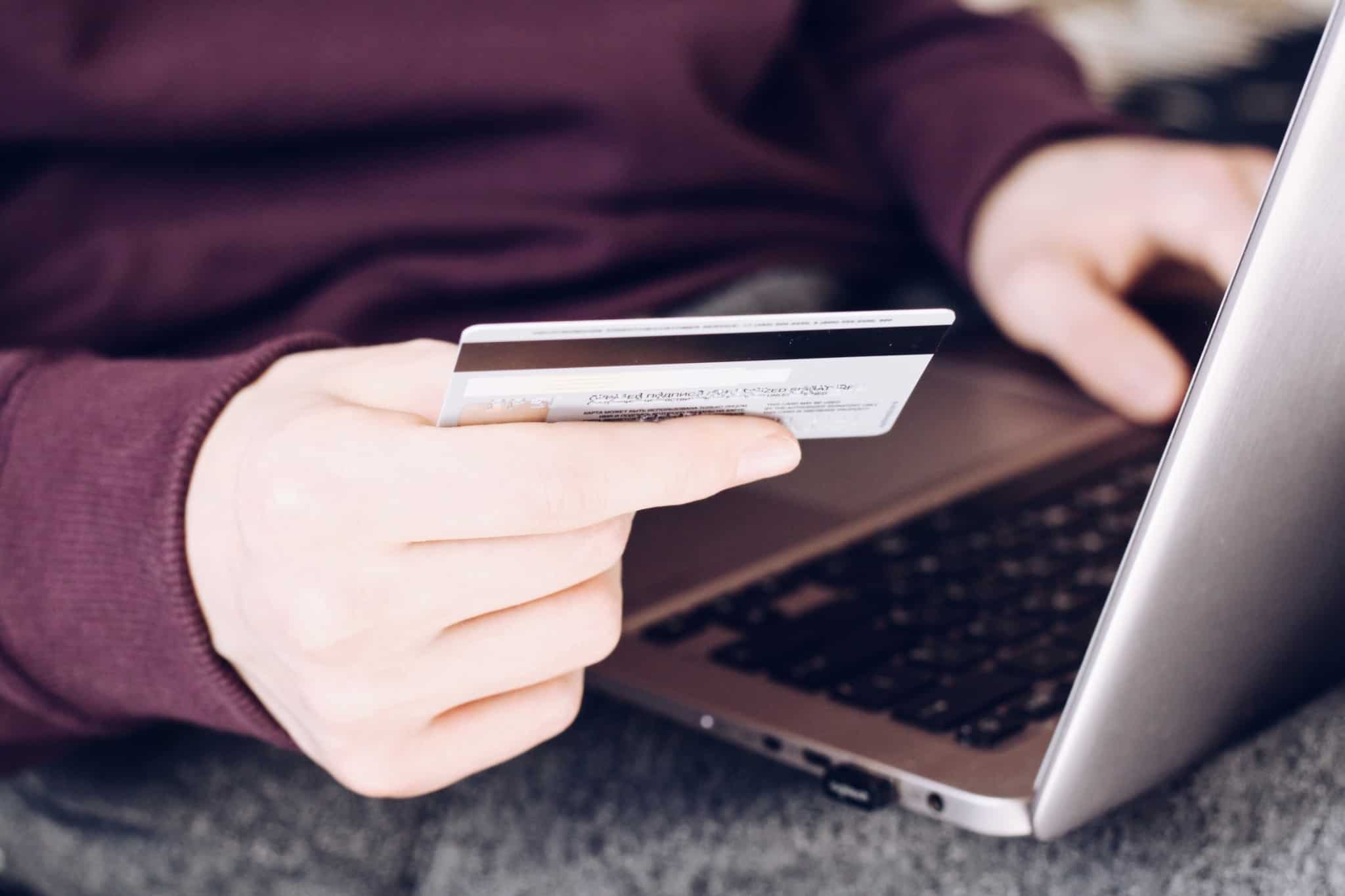 Homem com um cartão de crédito na mão a colocar os dados num site que está a consultar através do seu computador