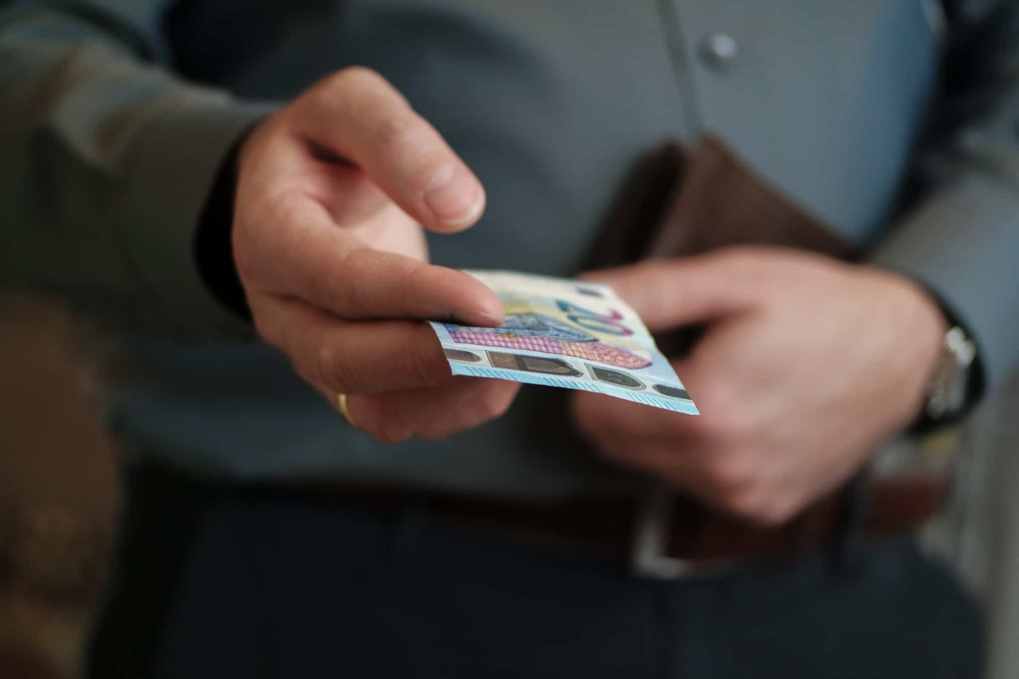 jovem homem segura carteira e estende nota de 20 euros, ilustrando o PIB e o seu peso no dia a dia