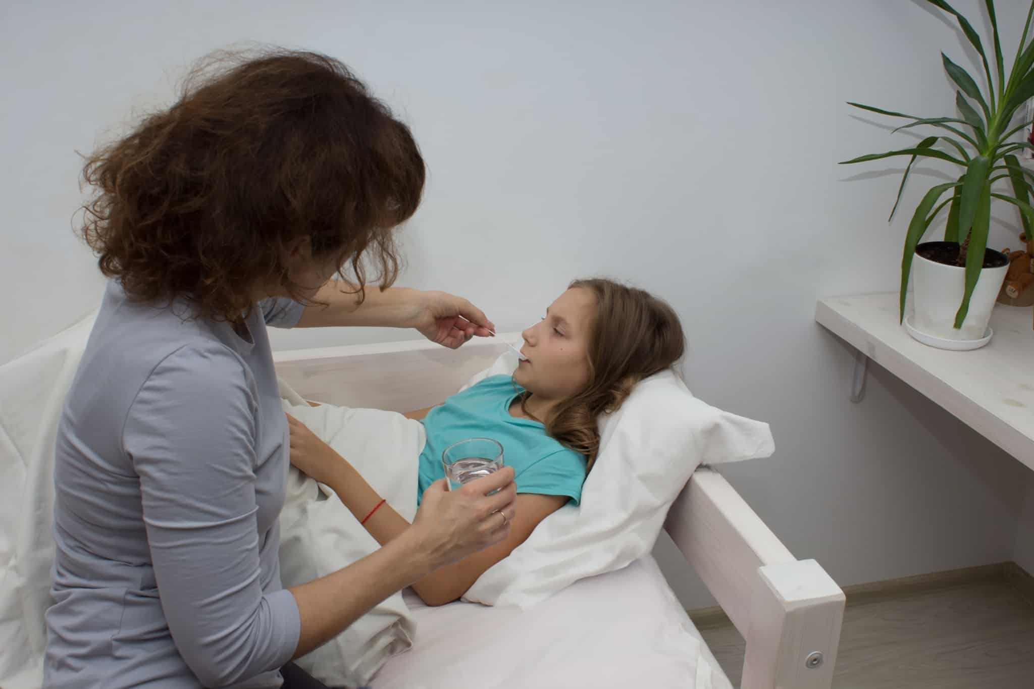 jovem mãe sentada à beira da cama da filha menor presta assistência usufruindo de baixa de apoio à família