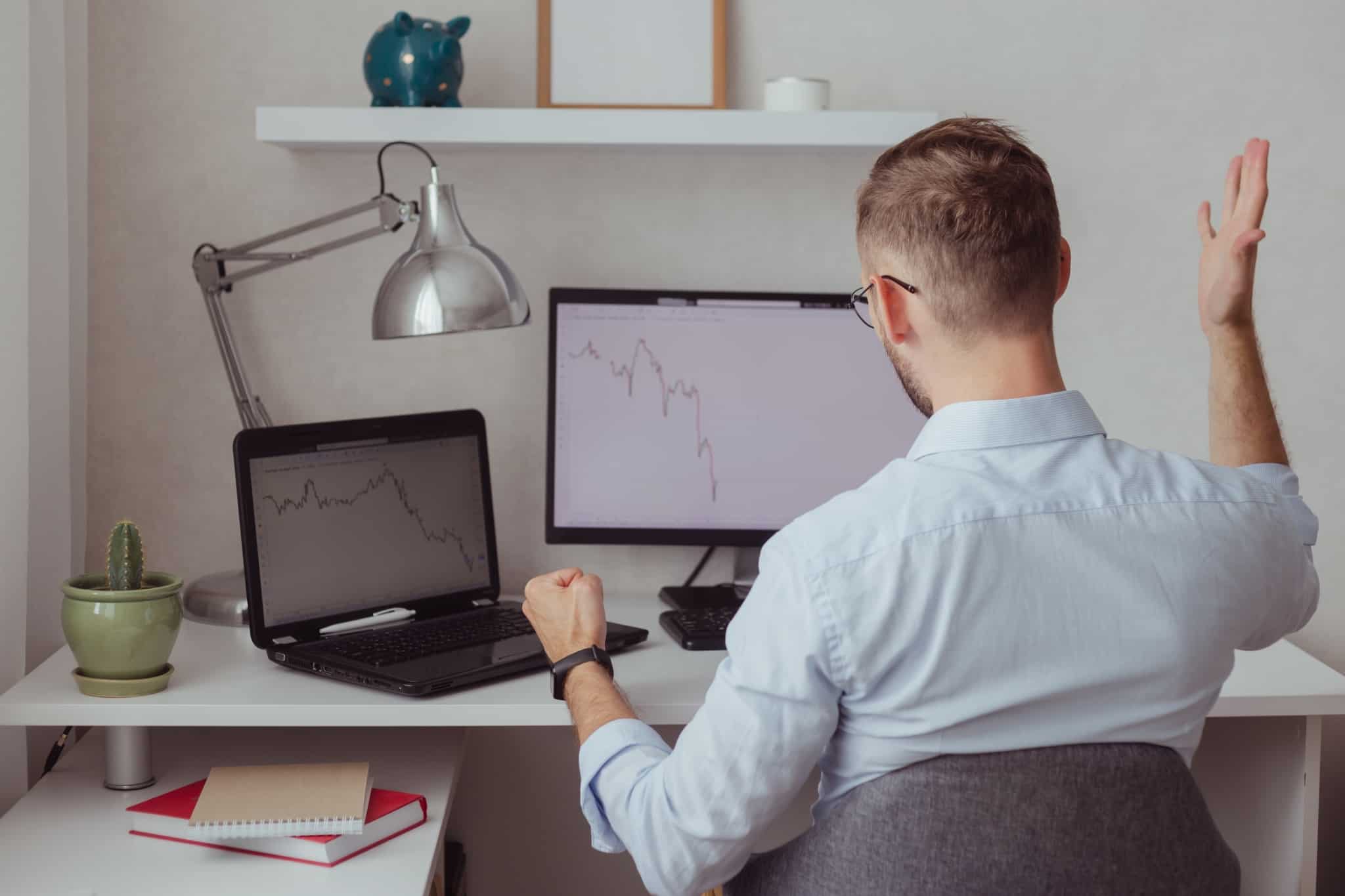 jovem rapaz investidor, a expressar a sua ansiedade e descontentamento, ao analisar os gráfcios dos mercados de valores em queda continuada hã algum tempo, ou seja, um bear market