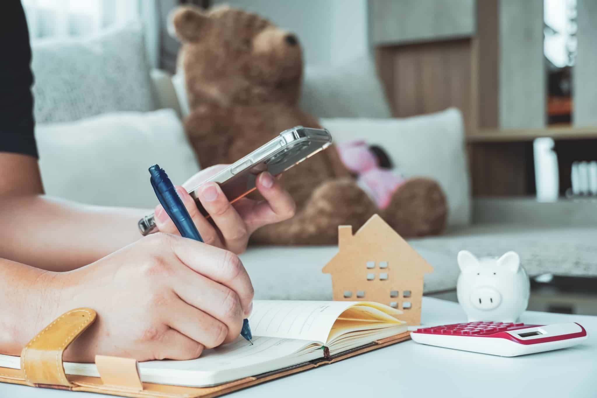 Homem a fazer contas no seu telemóvel e escrevendo no seu bloco sobre a compra de uma casa
