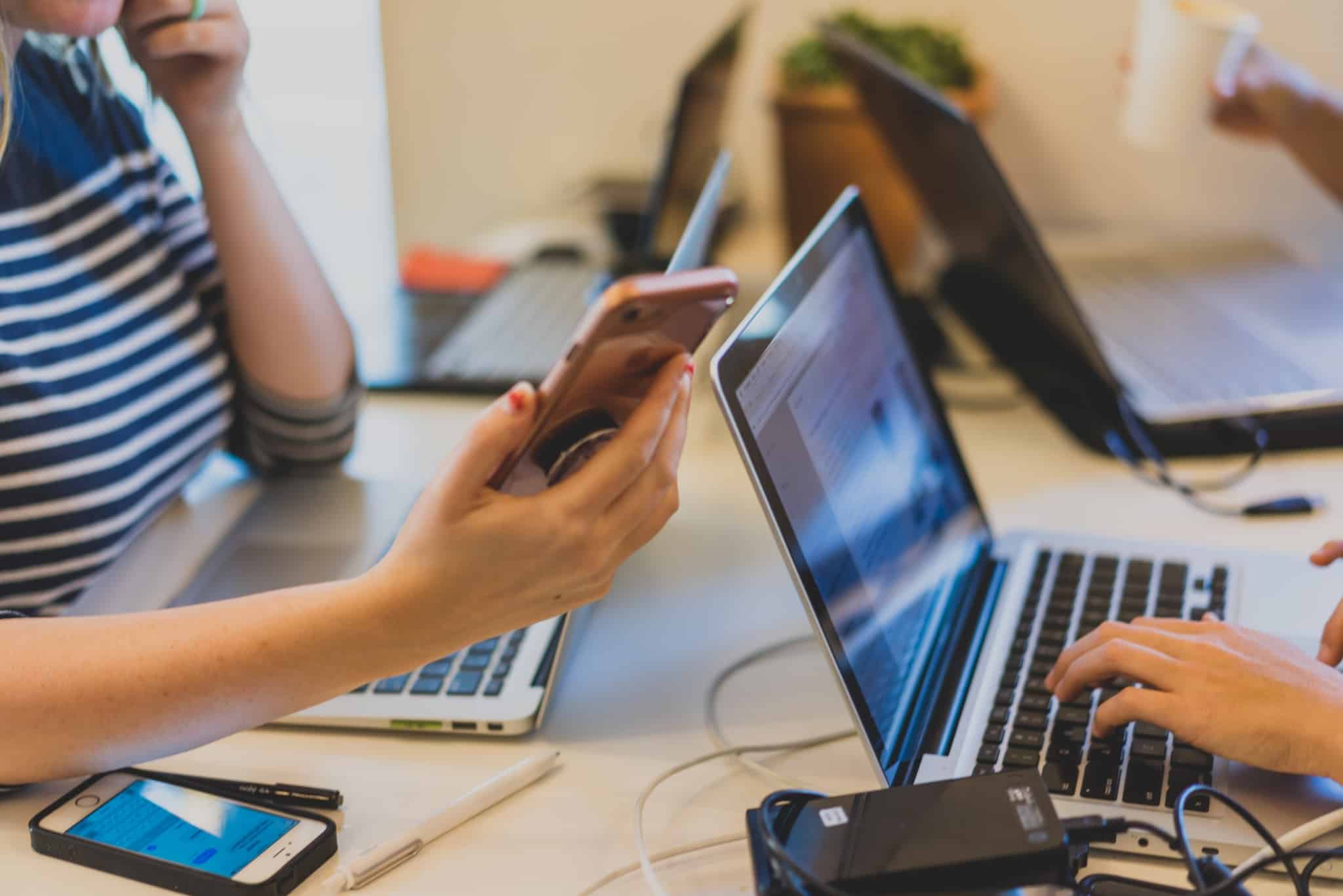 Mesa com alunos do Ensino Superior ao computador e rapariga a segurar em telemóvel