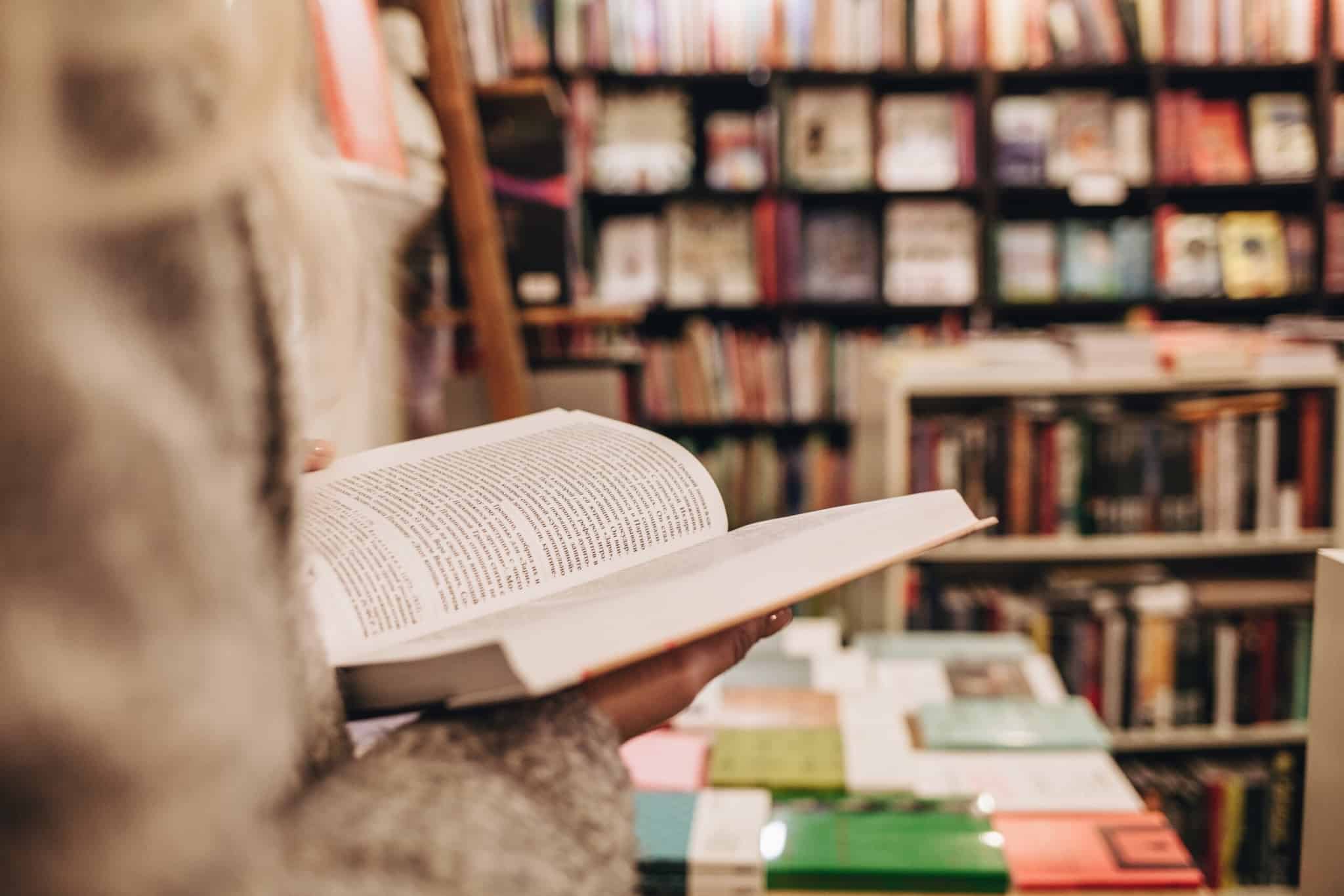 pessoa segura em livro aberto, o qual tem preço fixo, em ambiente de livraria