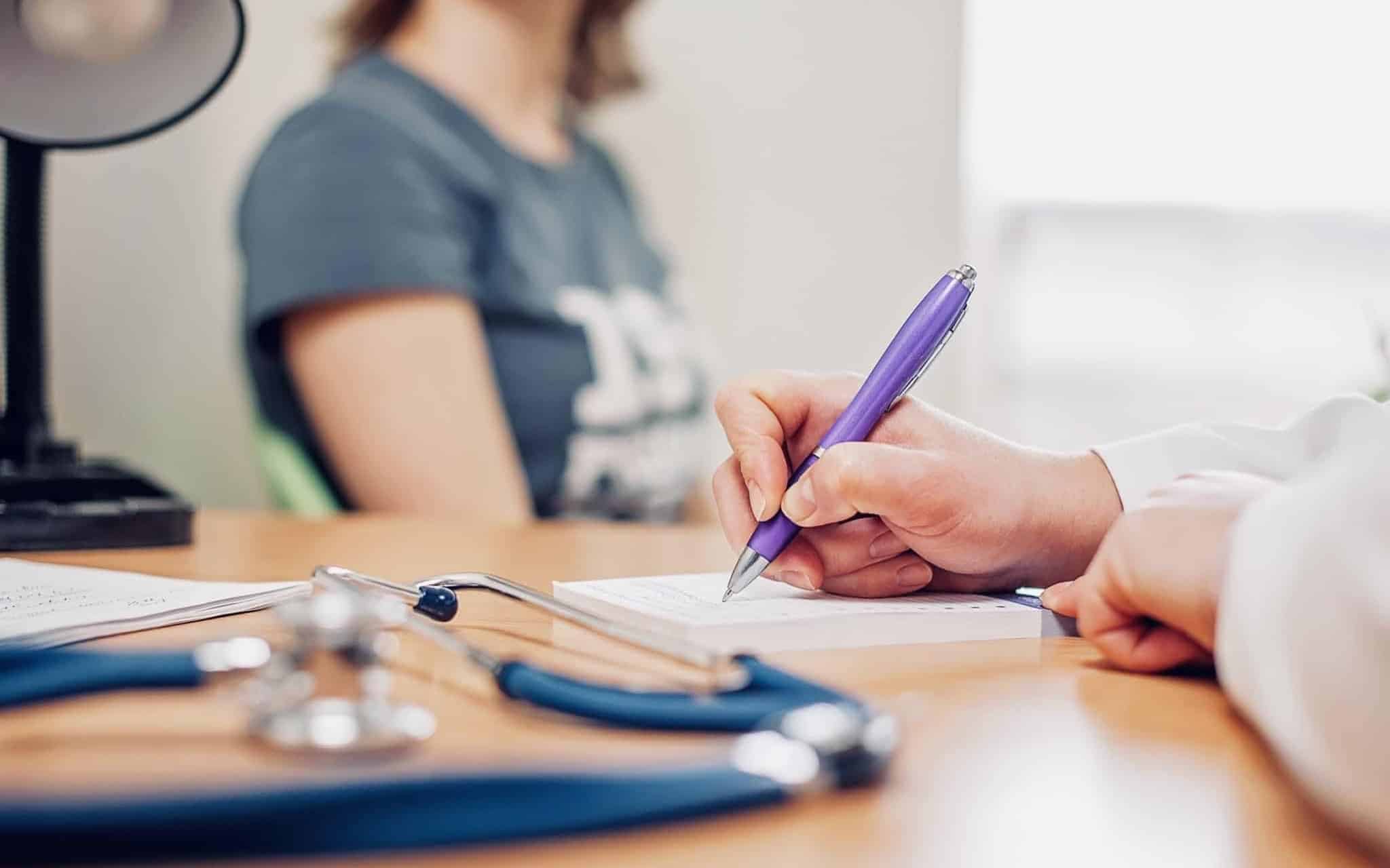 jovem mulher em consulta médica aguarda a prescrição que o médico está a redigir