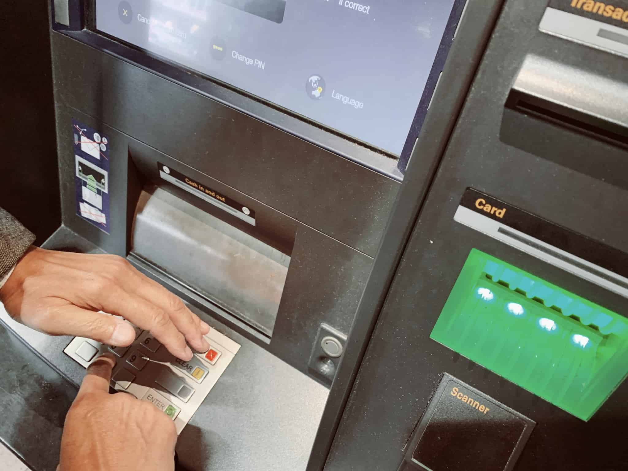 mão de homem numa caixa multibanco estrangeira tenta tapar o digitar do código para evitar as burlas ao usar cartão de crédito nas férias