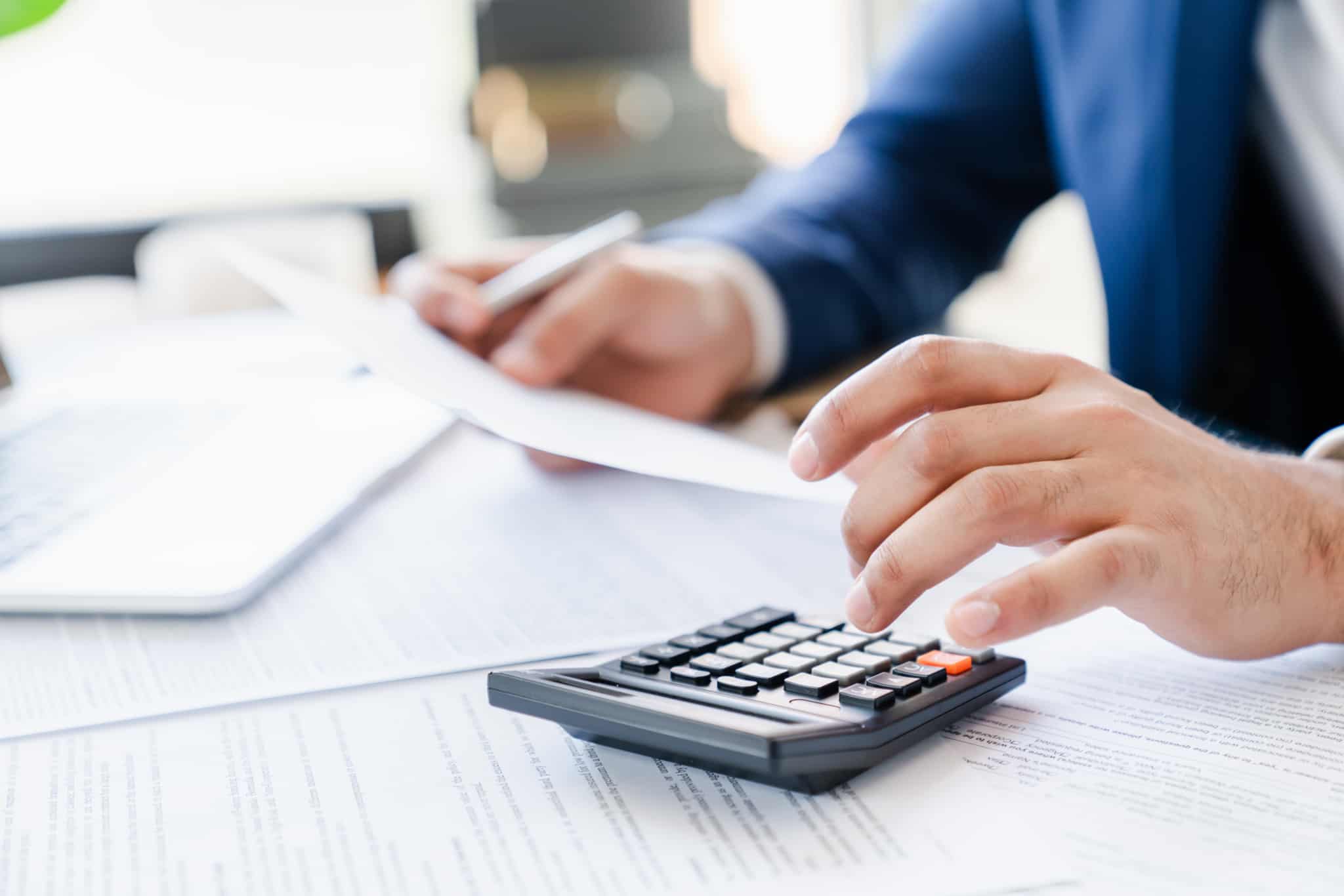 Homem a fazer contas numa calculadora pousada numa pilha de papéis