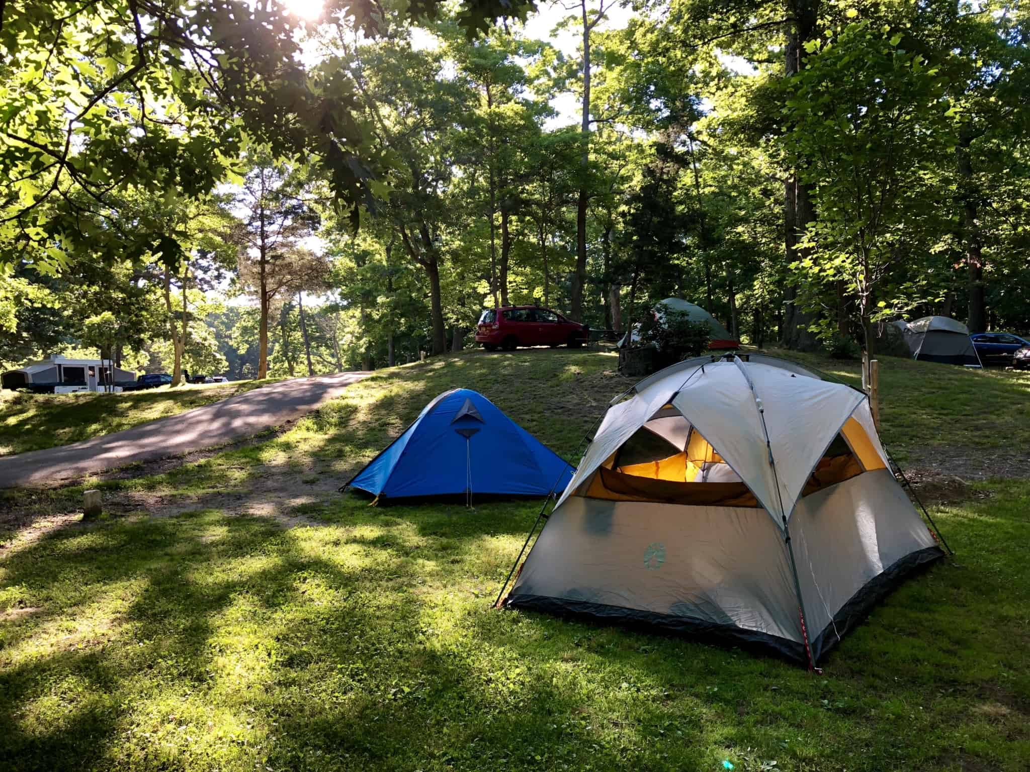 Tenda montada num parque de campismo rodeada de campo verde e árvores a fazerem sombra